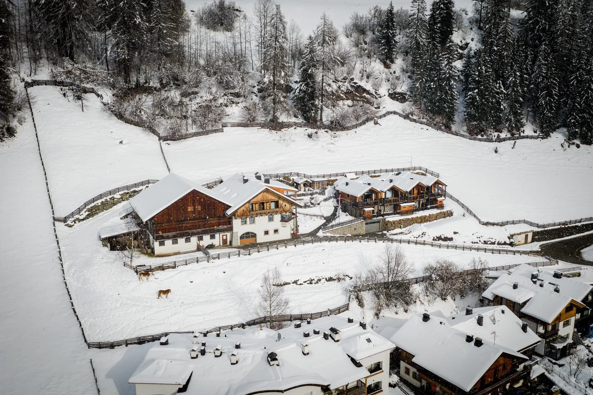 Das Bauernhaus des Stabinger Hof im Winter von oben, links der Holzgiebel des Wirtschaftsteils, rechts die Chalets, im Hintergrund der Wald.
