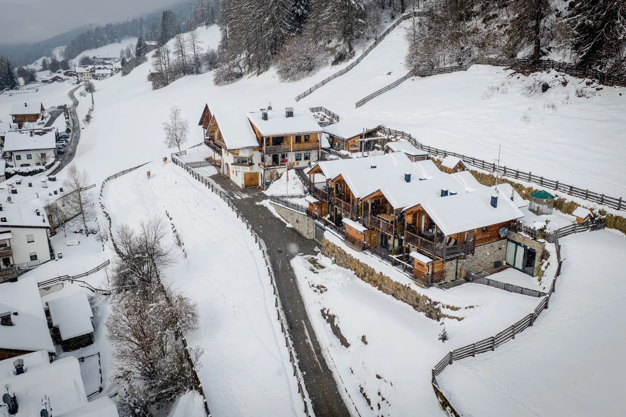 Blick aus der Luft den Hang hinunter auf den Stabinger Hof, davor die geräumte Straße und die Dächer der Nachbarhäuser unter Schnee.