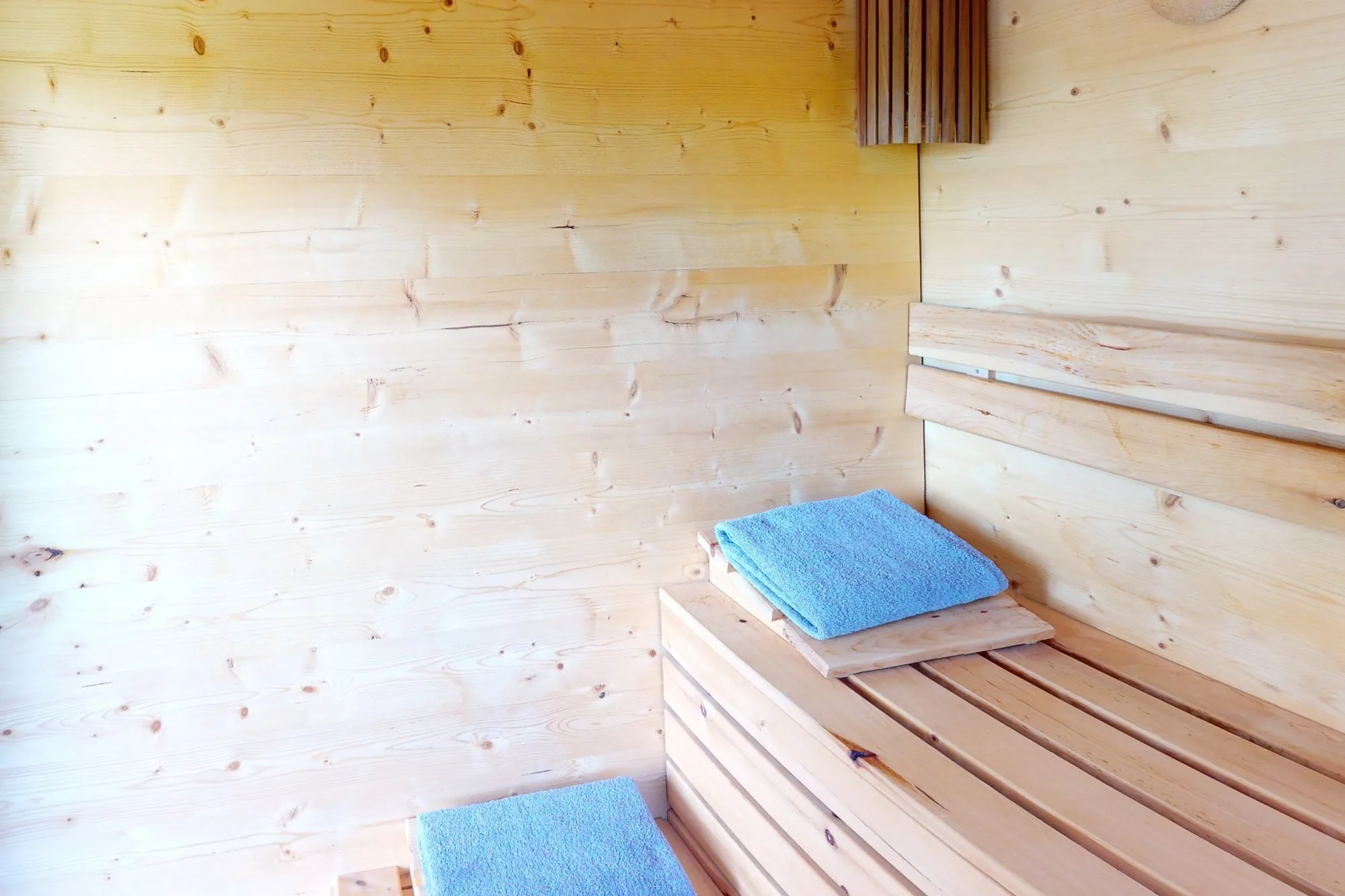 Die Sauna einer Einheit: Bänke aus hellem Holz mit zwei blauen Tüchern, rechts der Ofen hinter einem Gitter.