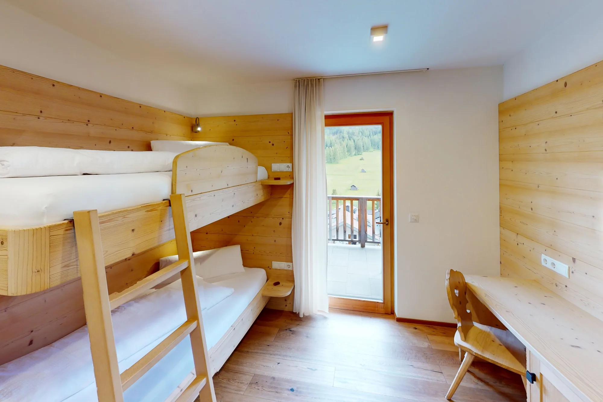 Ein Zimmer mit Stockbett aus hellem Holz und Leiter, rechts ein Schreibtisch, dahinter die Fenstertür auf den Balkon.