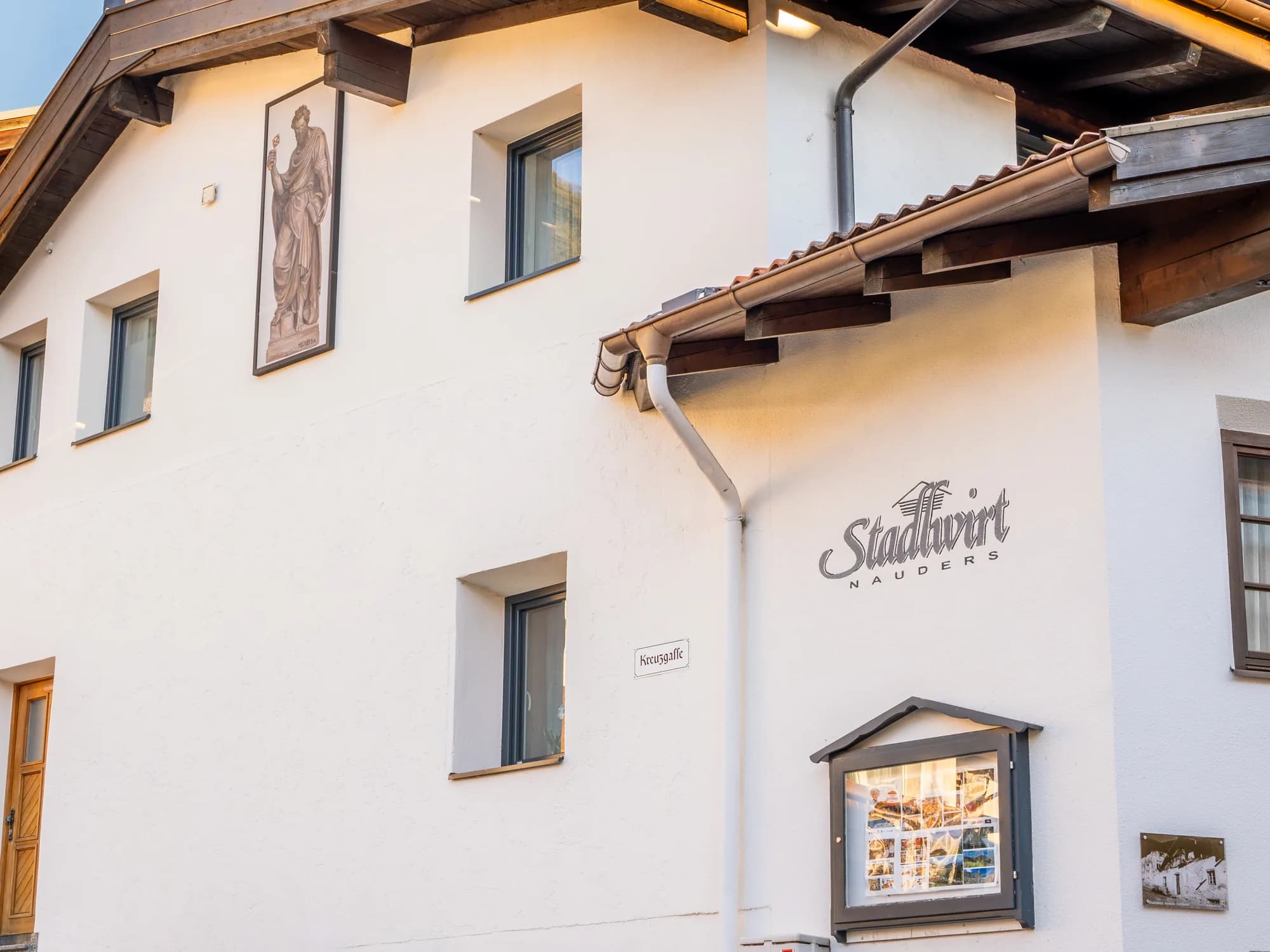 Die Fassade des Stadlwirt in Nauders: der gemalte Schriftzug Stadlwirt auf der weißen Wand, daneben ein Fresko und der Schaukasten neben dem Fenster.