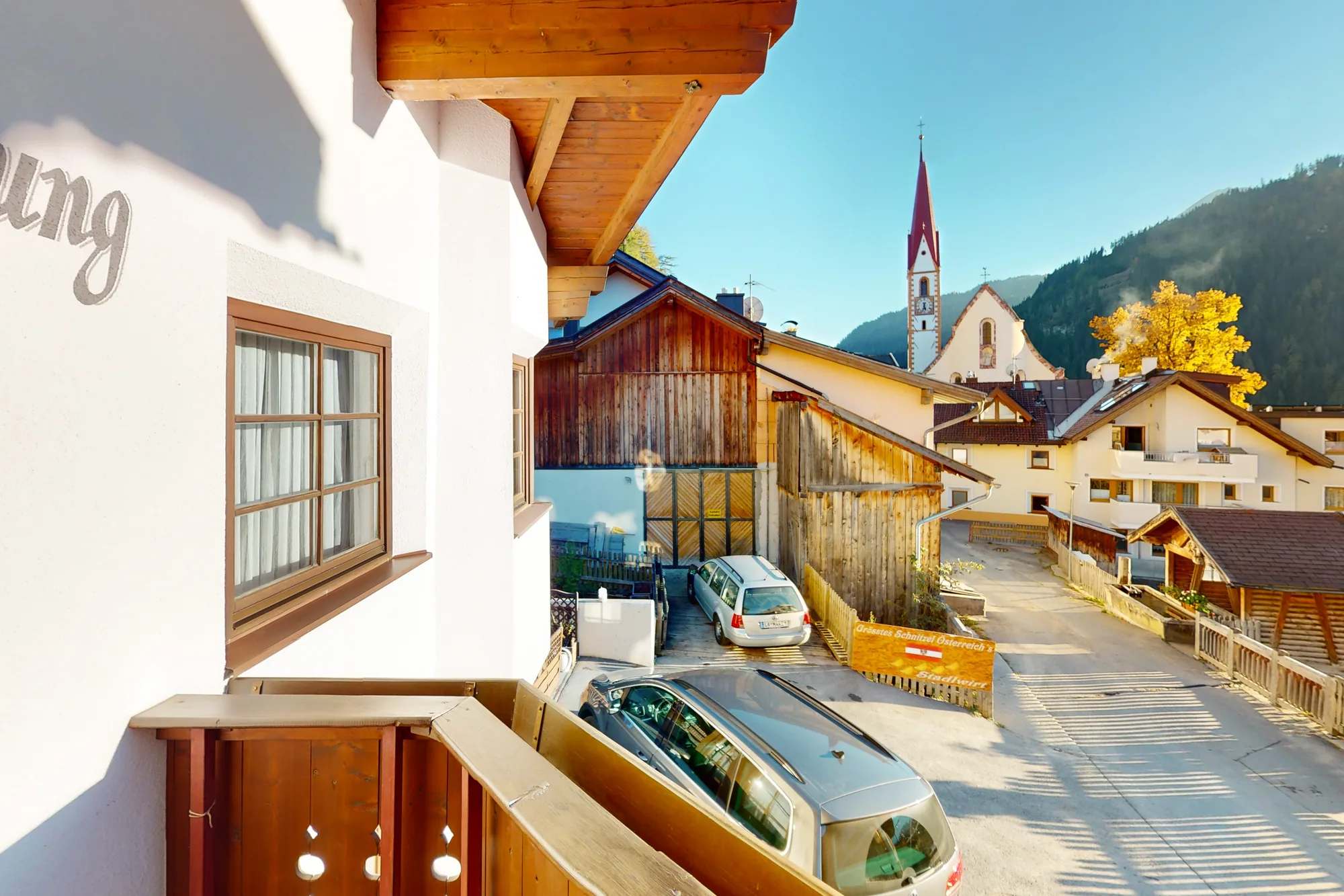 Der Blick vom Balkon des Stadlwirt über die Dorfstraße von Nauders: alte Holzstadel und weiße Häuser beidseits, am Ende der Kirchturm vor dem bewaldeten Hang.