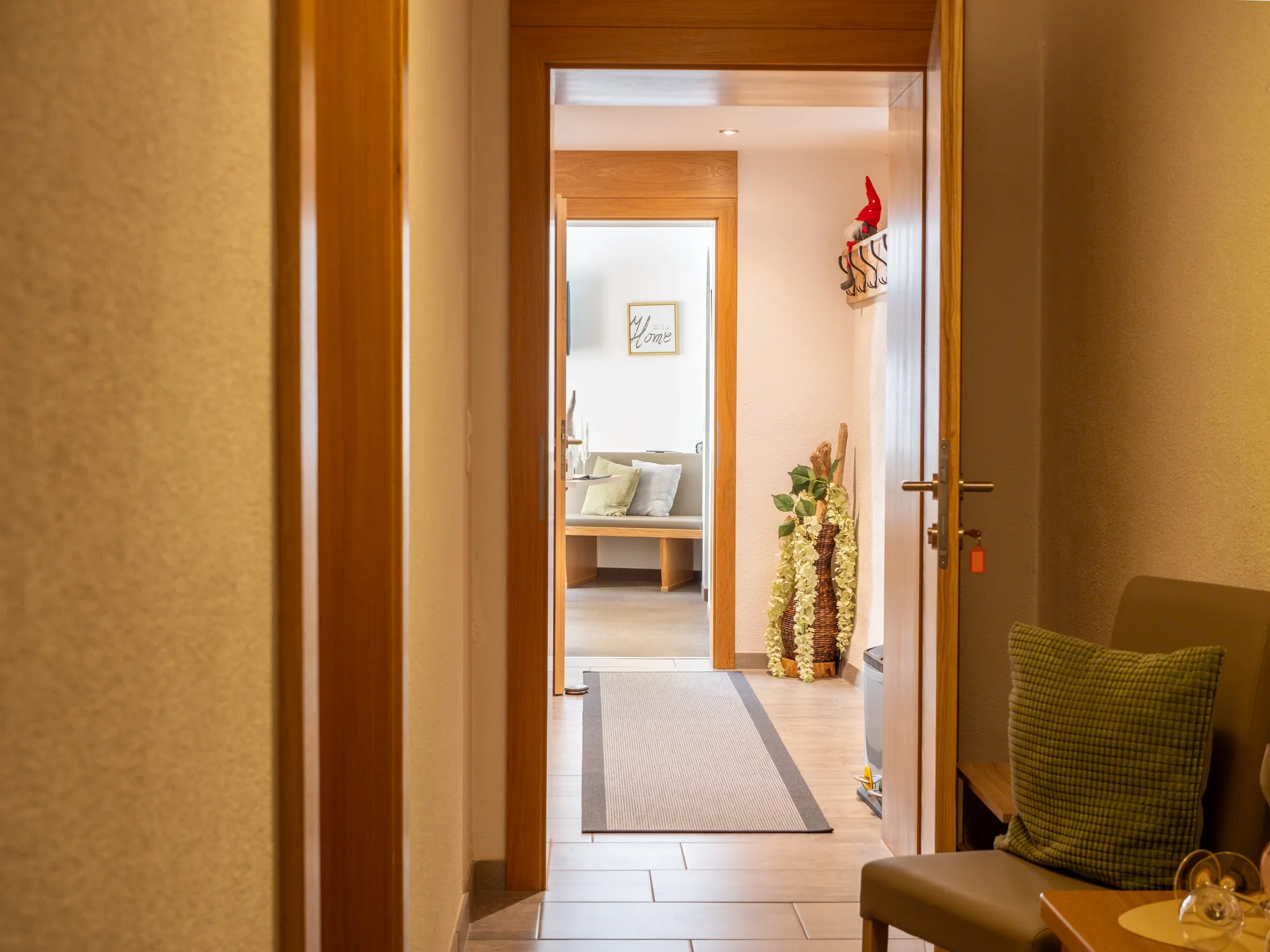 Der Gang der Wohnung Hias: ein heller Flur mit Läufer, rechts und links offene Holztüren, durch die ein Schlafzimmer und die Stube zu sehen sind.