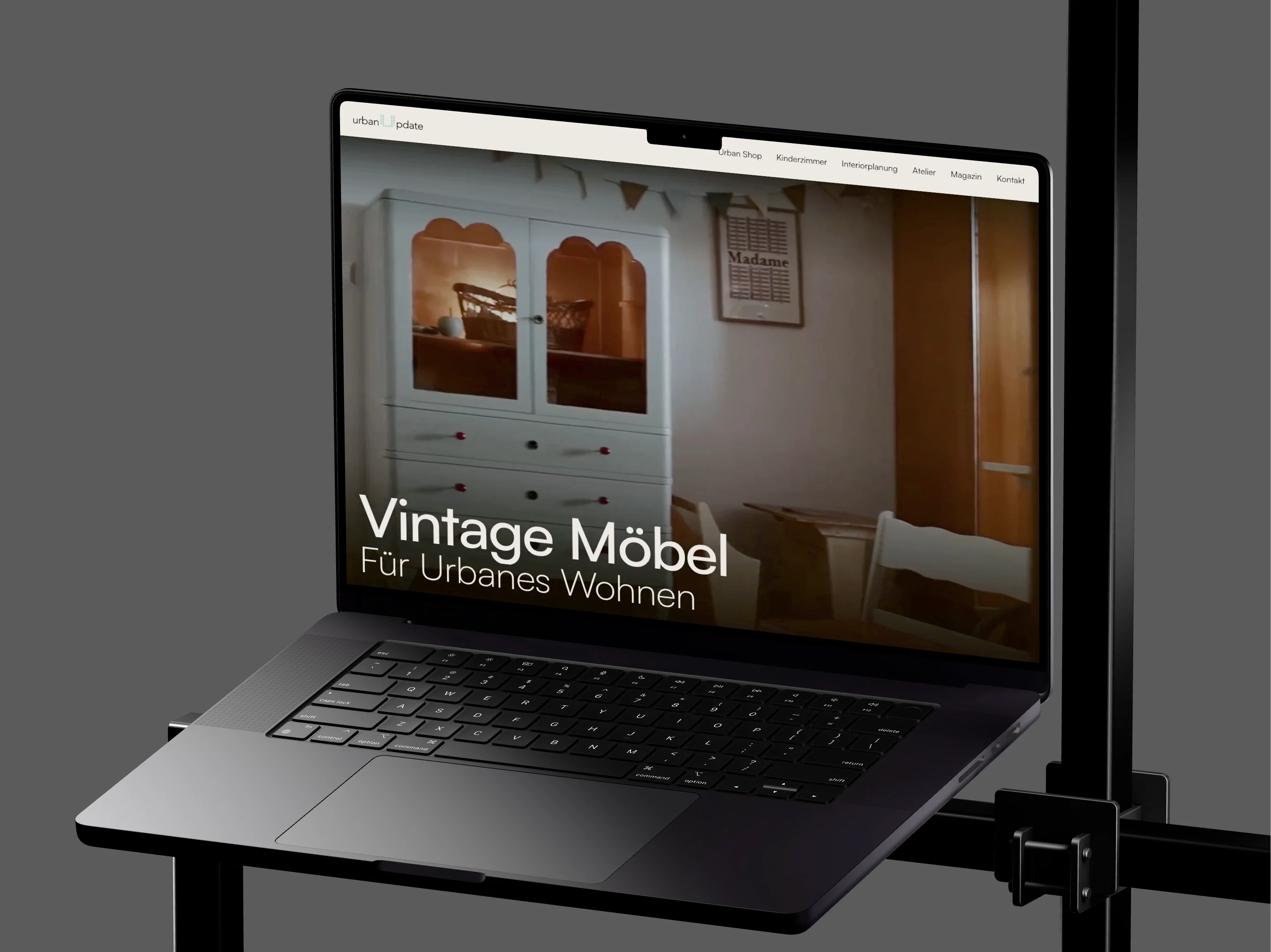 Ein MacBook Pro auf einem schwarzen Drahtgestell zeigt die Startseite von UrbanUpdate mit einem hellblauen Vintage-Kasten und der Zeile Vintage Möbel für urbanes Wohnen.