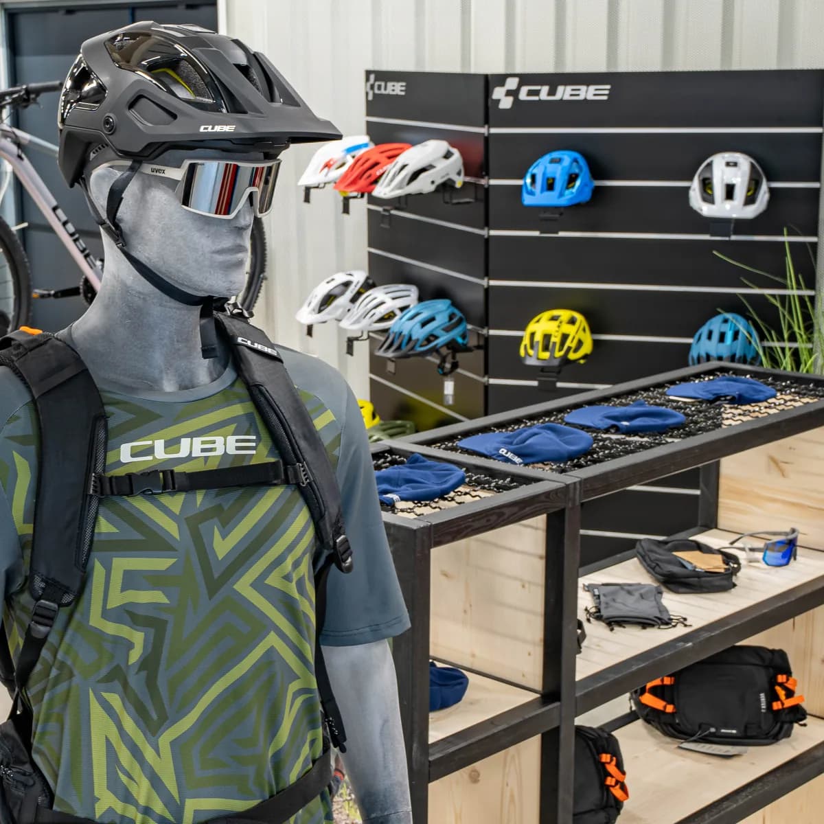 Helmwand im CUBE Store Goslar: Helme in mehreren Farben an einer Lochwand, davor eine Figur mit Rucksack und Helm.