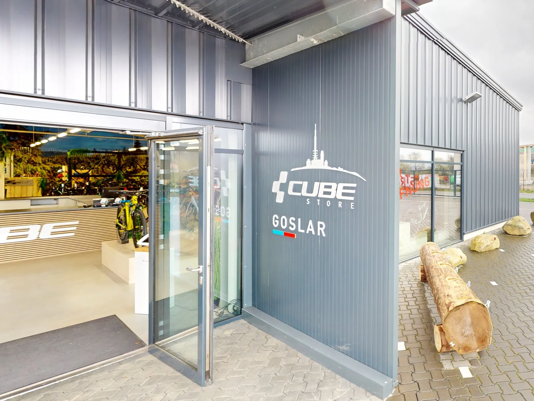 Der Eingang des CUBE Store Goslar: die offene Glastür in der grauen Fassade, daneben der Schriftzug CUBE Store Goslar, dahinter der Verkaufsraum mit den ersten Rädern.