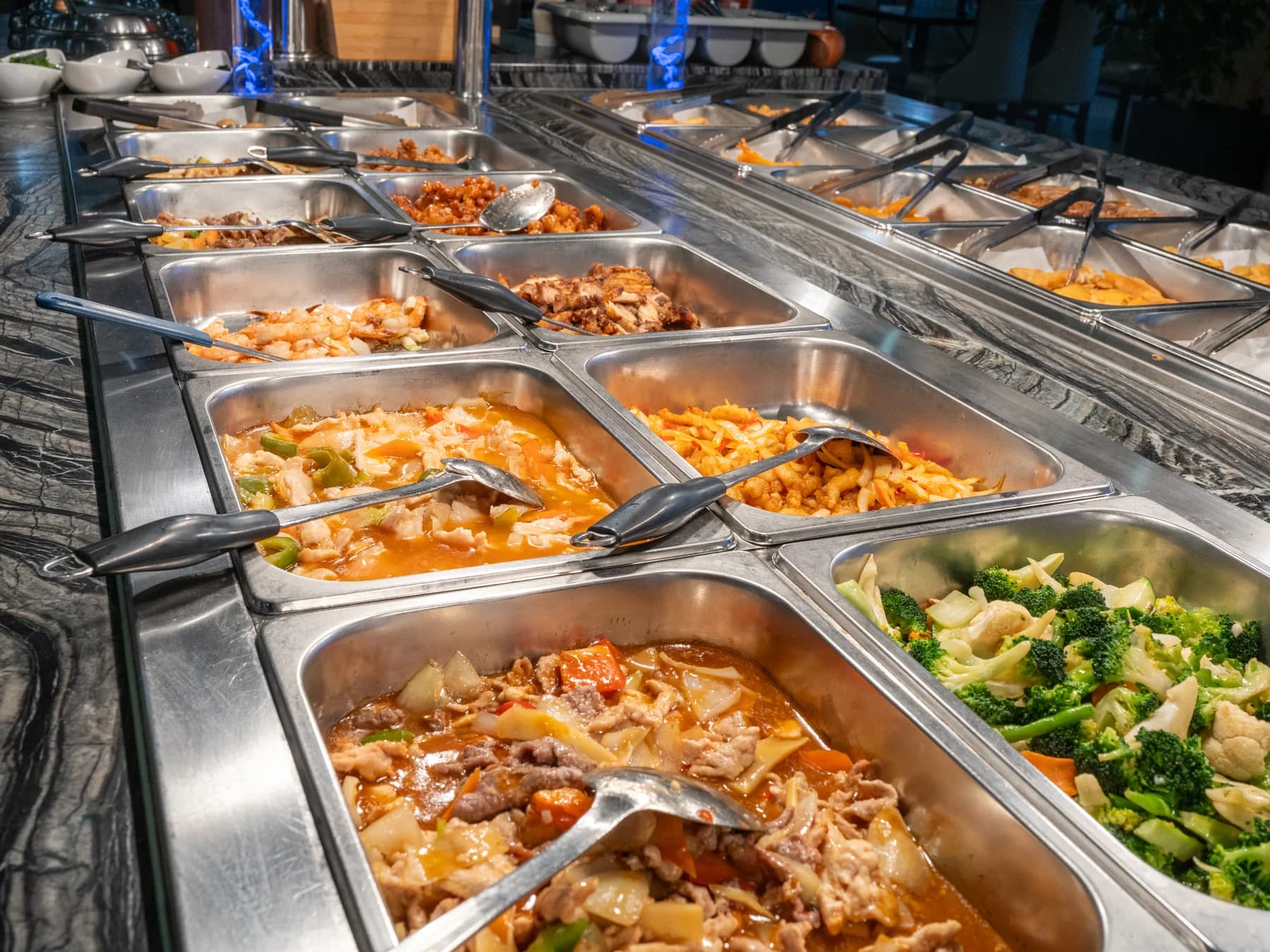 Die Wannen einer Buffetlinie mit Nudeln, Gemüse und Fleischgerichten, dazwischen Zangen und Löffel, die Reihe läuft in die Tiefe.