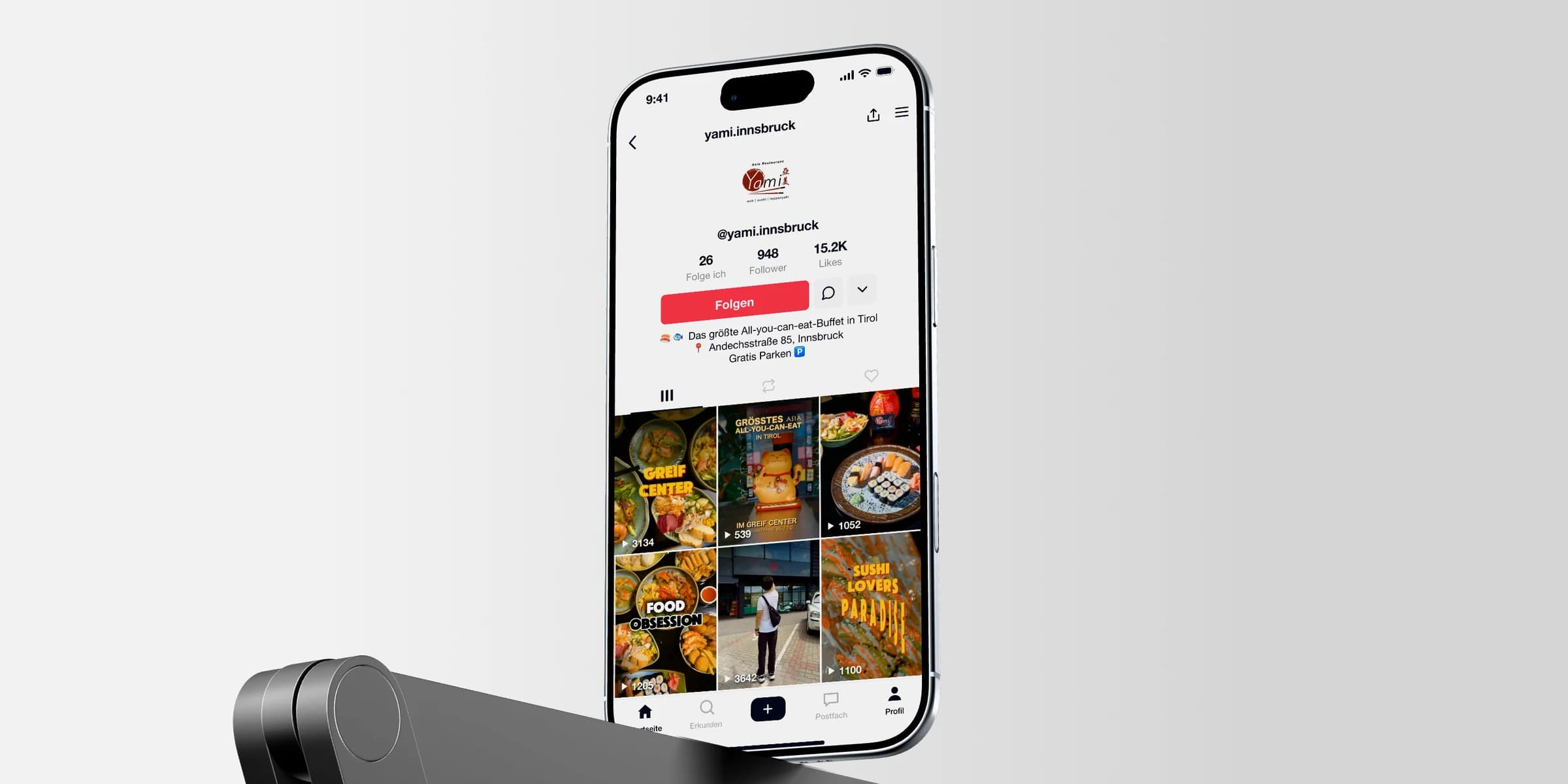 Asia Restaurant YAMI: Ein iPhone zeigt das TikTok-Profil mit dem Raster seiner Beiträge über einem Metallrahmen vor hellem Grund.