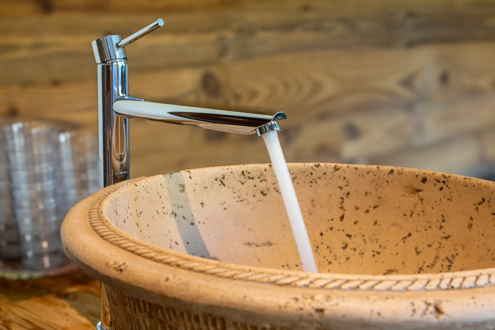 Ein steinernes Becken mit fließendem Wasser aus einem hohen Hahn, daneben ein Stapel Gläser auf der Holzablage.
