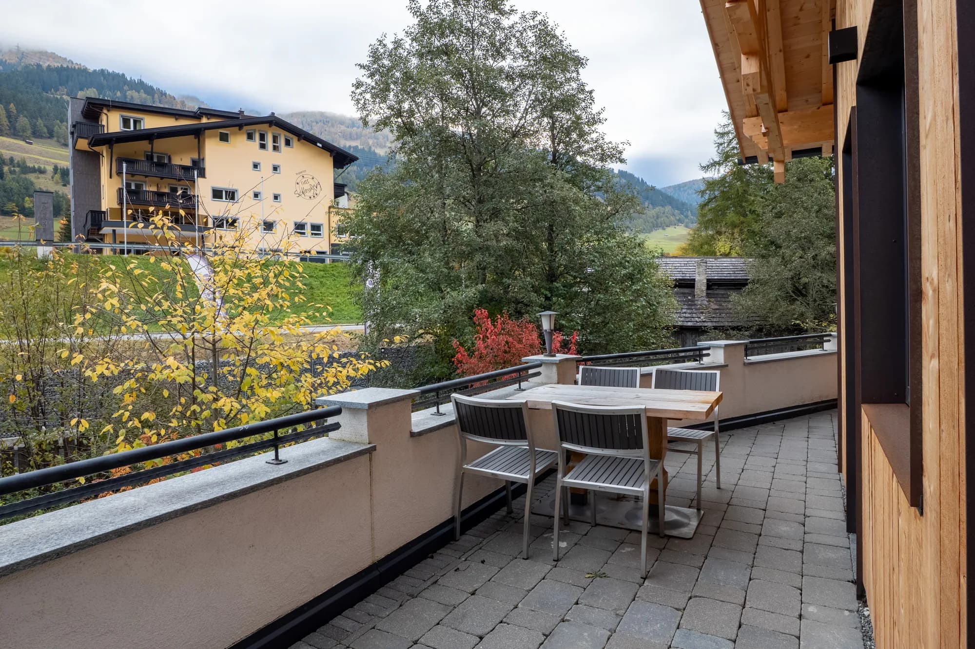 Die Terrasse des Blockhauses Fuchsbau: ein Holztisch mit Stühlen unter dem vorspringenden Dach, dahinter der Blick über die Häuser von Nauders auf den bewaldeten Hang.