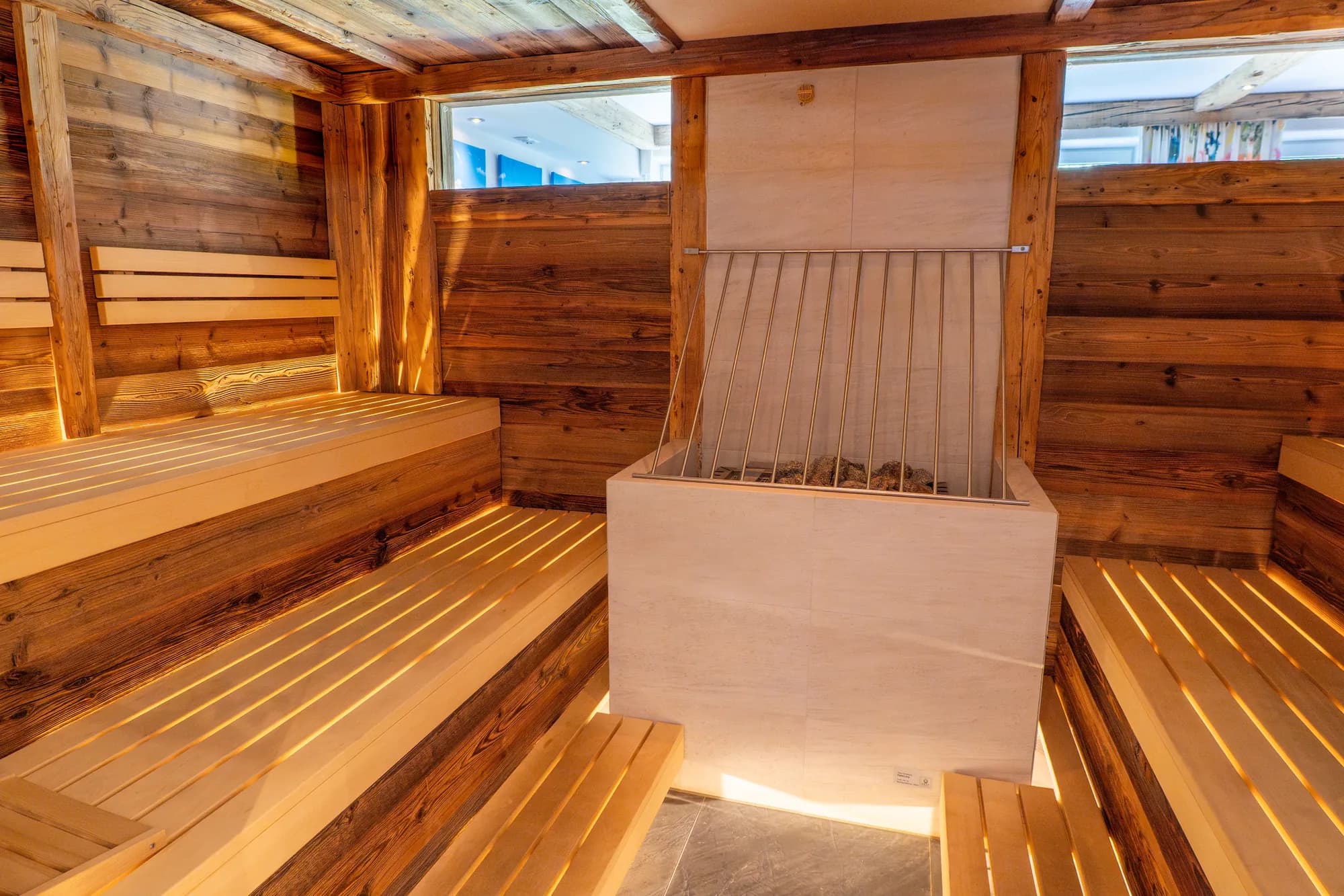 Die Stubensauna der Alten Mühle: Bänke und Wände aus dunklem Altholz, eine helle Rückenlehne in der Mitte, oben ein schmales Fenster ins Freie.