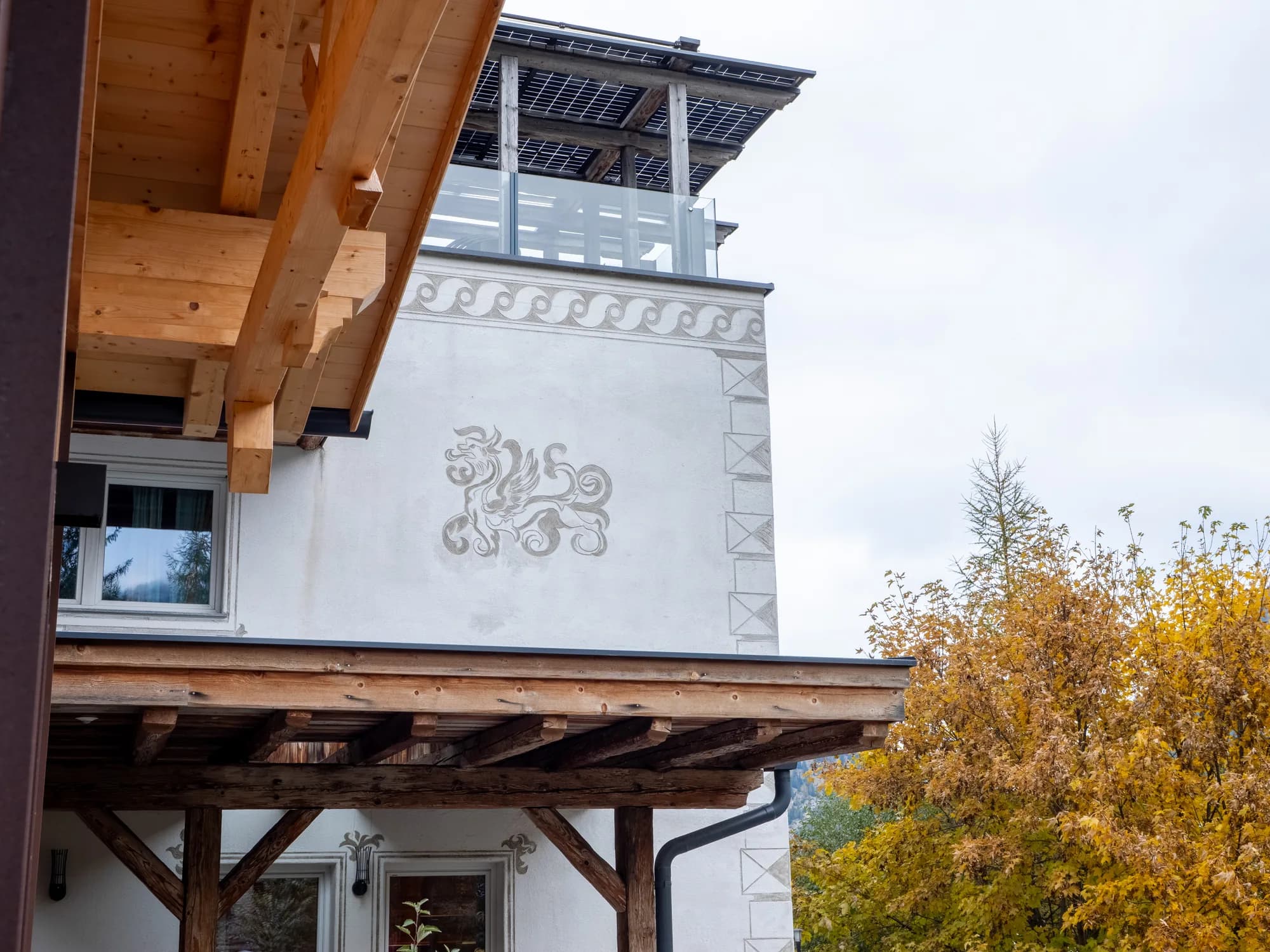 Die Fassade der Alten Mühle in Nauders: ein gemaltes Sgraffito auf der weißen Wand über dem Eingang, darüber der Holzbalkon und das vorspringende Vordach.