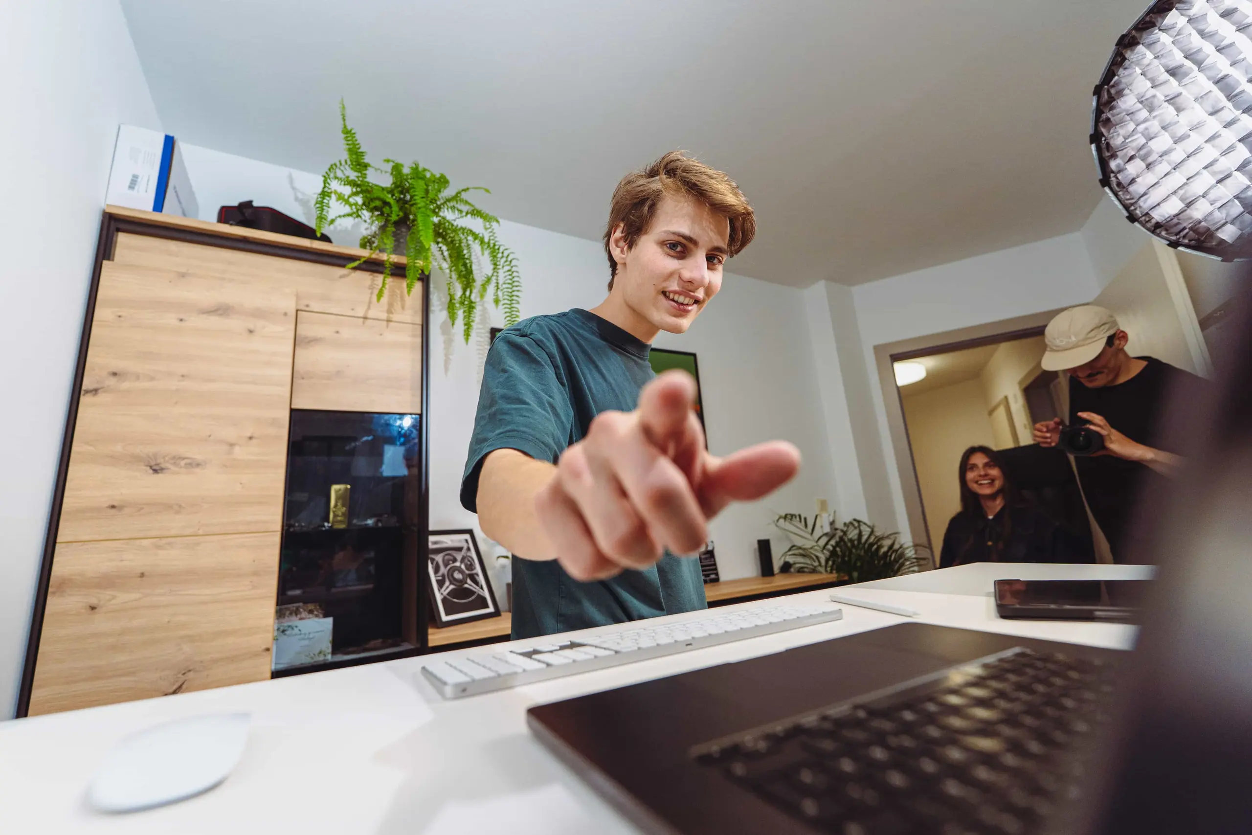 Mitarbeiter von Invisions am Schreibtisch im Innsbrucker Büro, zwei Kolleginnen und Kollegen im Türrahmen dahinter.