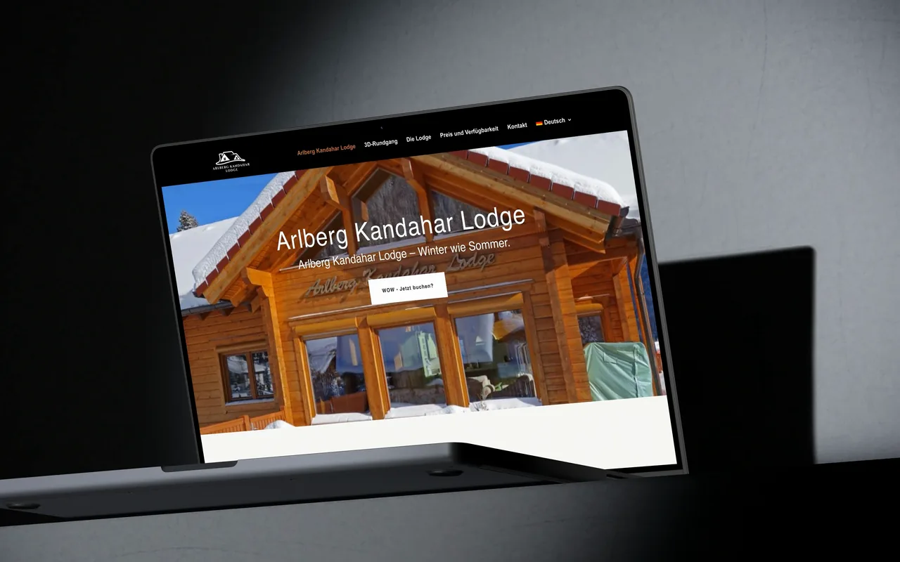 Ein MacBook im Lichtkegel zeigt arlbergkandaharlodge.at: zuerst nah die Startseite mit dem verschneiten Holzchalet, dann das ganze Gerät, während die Seite bis zur Buchungsanfrage durchläuft.