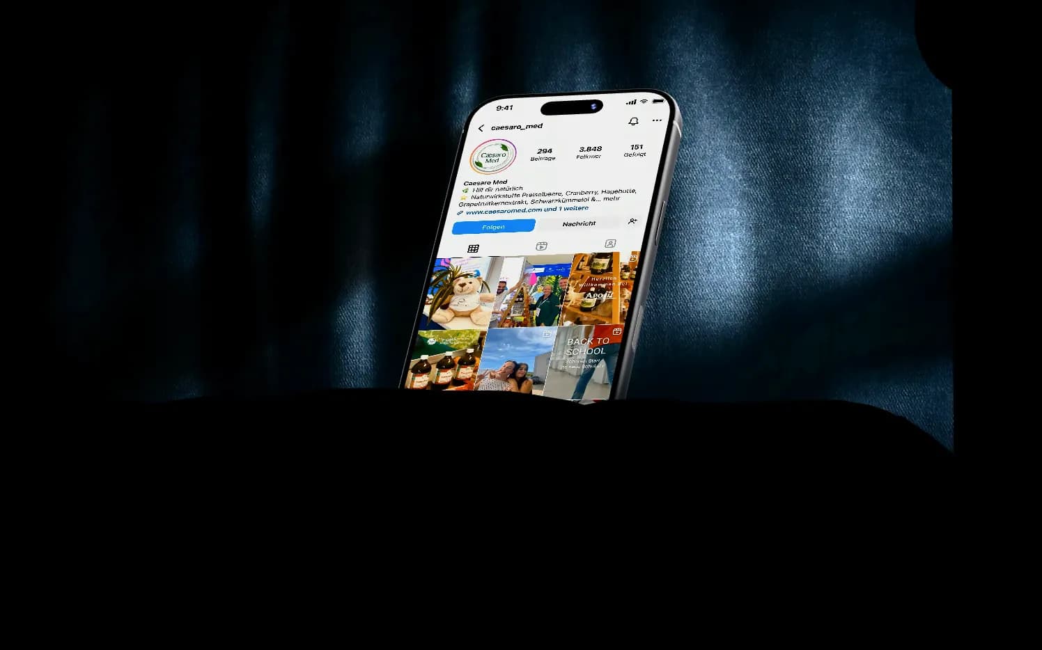 Ein iPhone auf dunklem Stoff zeigt das Instagram-Profil von Caesaro Med: erst das Profil, dann das gescrollte Beitragsraster, dann zwei laufende Reels.