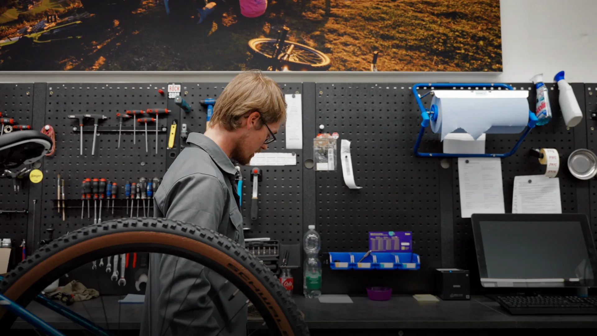 Ausschnitt aus dem Film über den Servicetermin: ein Mitarbeiter zeigt in der Werkstatt einen abgenutzten Zahnkranz und danach ein Rad im Montageständer.