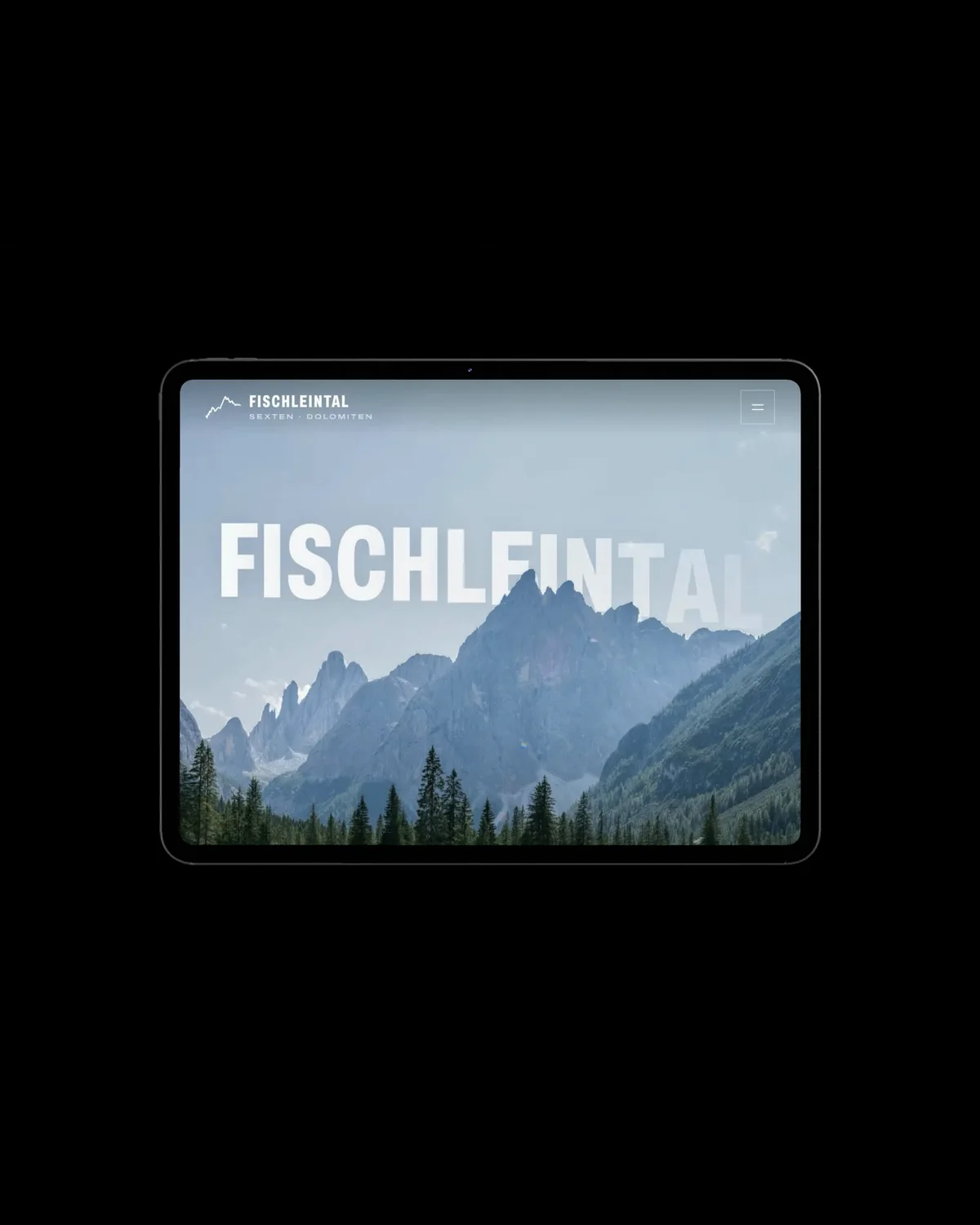 Ein iPad quer im Dunkeln zeigt die Startseite von fischleintal-dreizinnen.it mit dem Schriftzug Fischleintal über den Bergen.