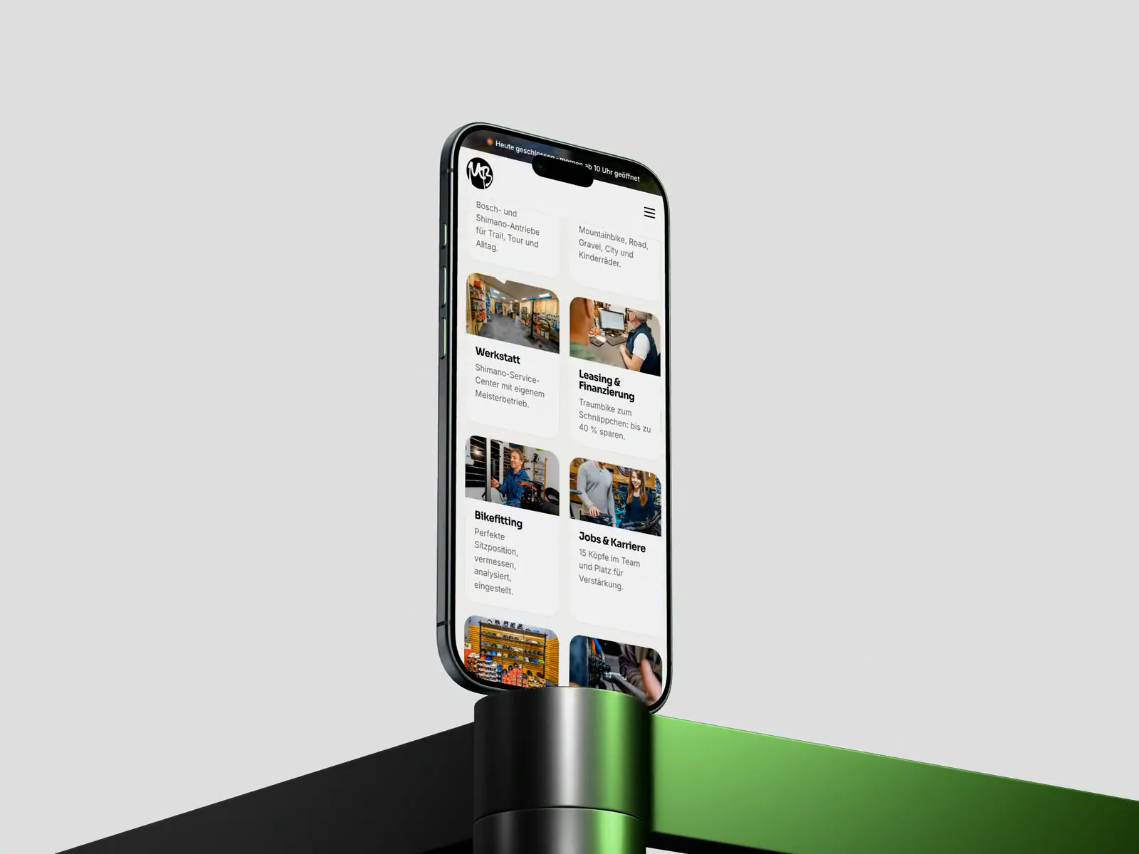 Ein iPhone auf einem Sockel vor hellem Grund zeigt die mobile Fassung von mr-bike.de mit den Kacheln für Werkstatt, Leasing und Bikefitting.