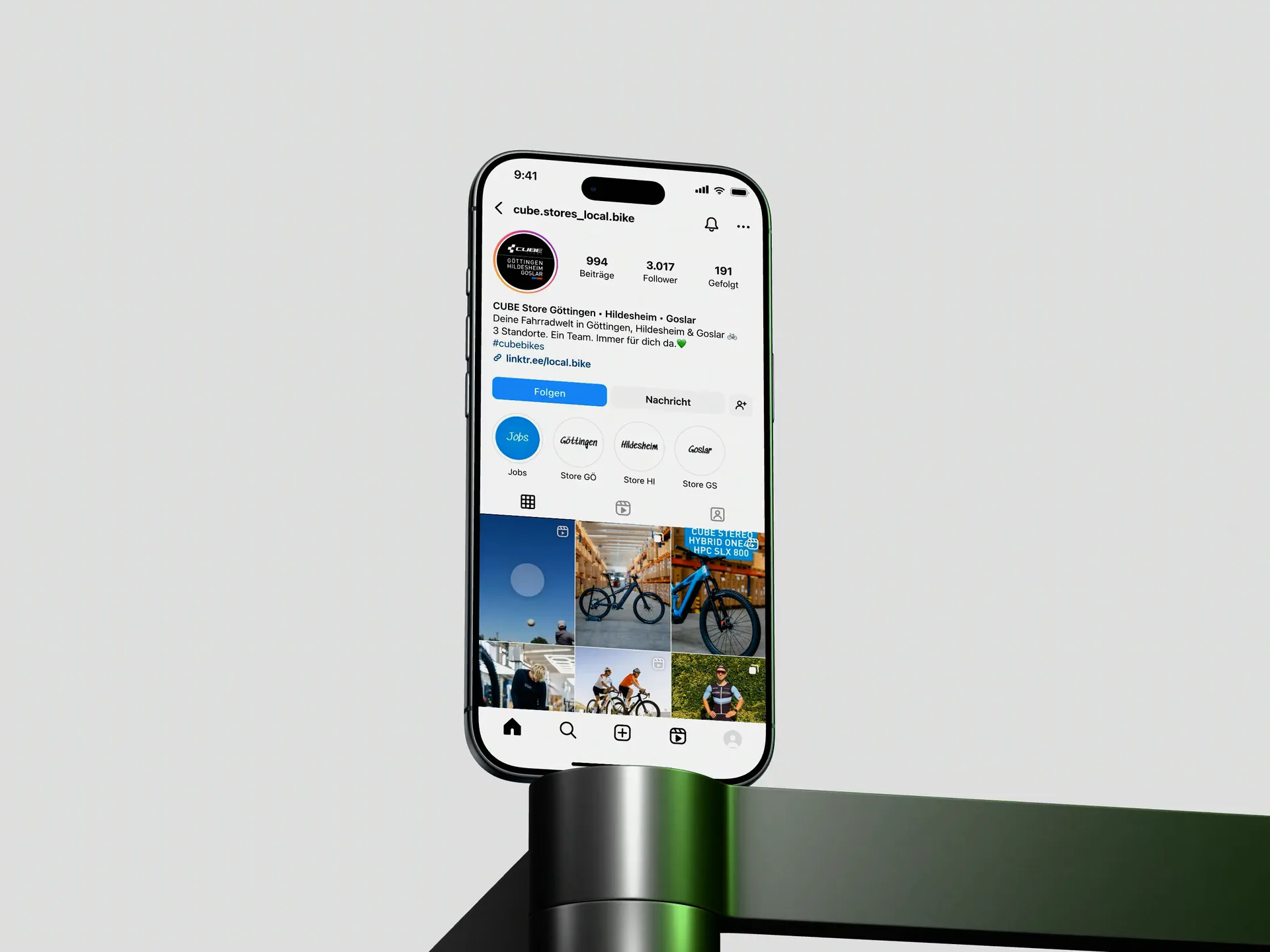 Ein iPhone Air steht auf einem schwarzgrünen Halter vor hellem Grund und zeigt das Instagram-Profil der CUBE Stores, danach zwei Reels mit Detailaufnahmen eines Rennrads.