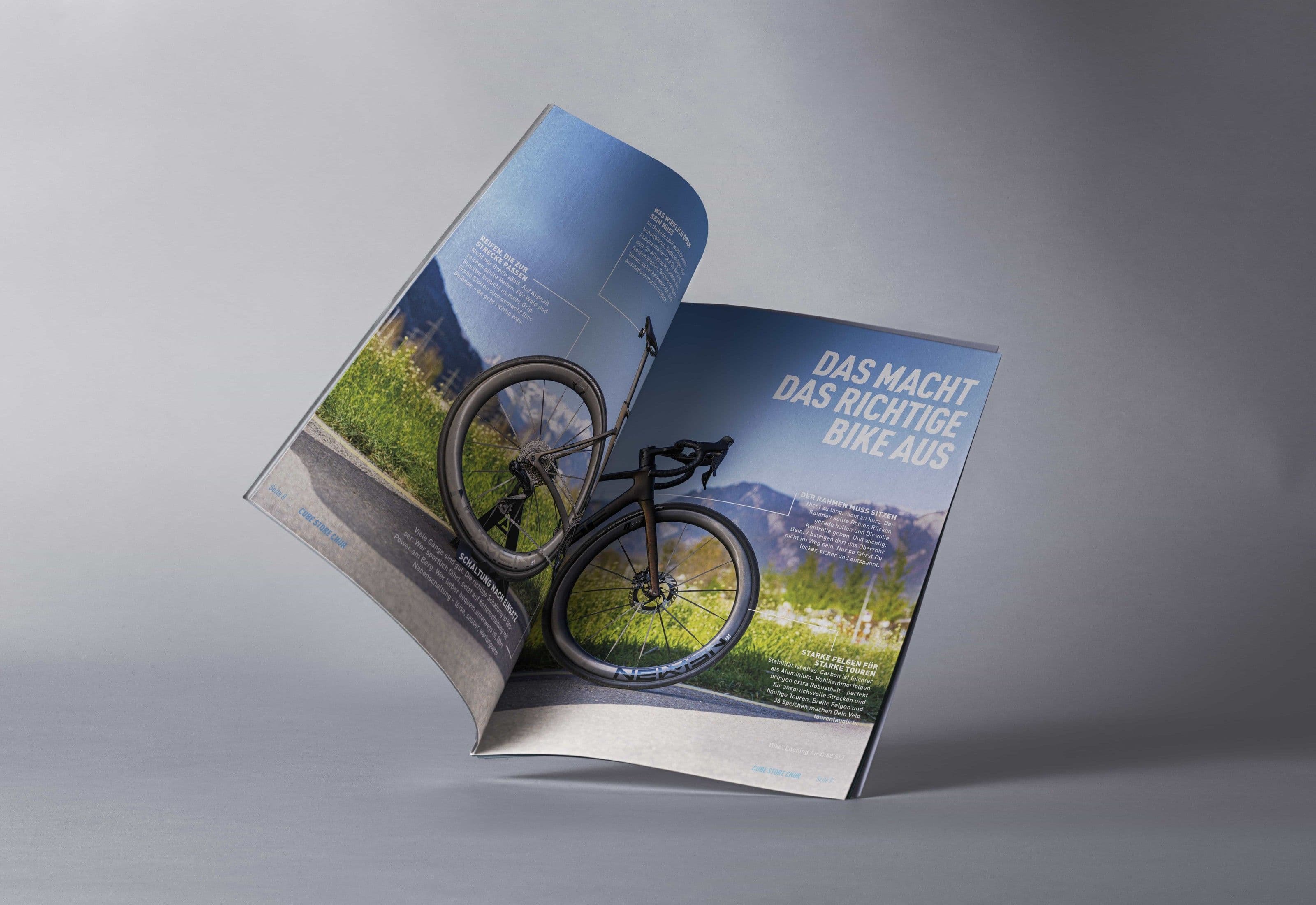 Ein freistehend gebogenes A4-Heft vor grauem Verlauf, aufgeschlagen auf der Doppelseite DAS MACHT DAS RICHTIGE BIKE AUS mit einem freigestellten Gravelbike und Linien zu kurzen Fachtexten.