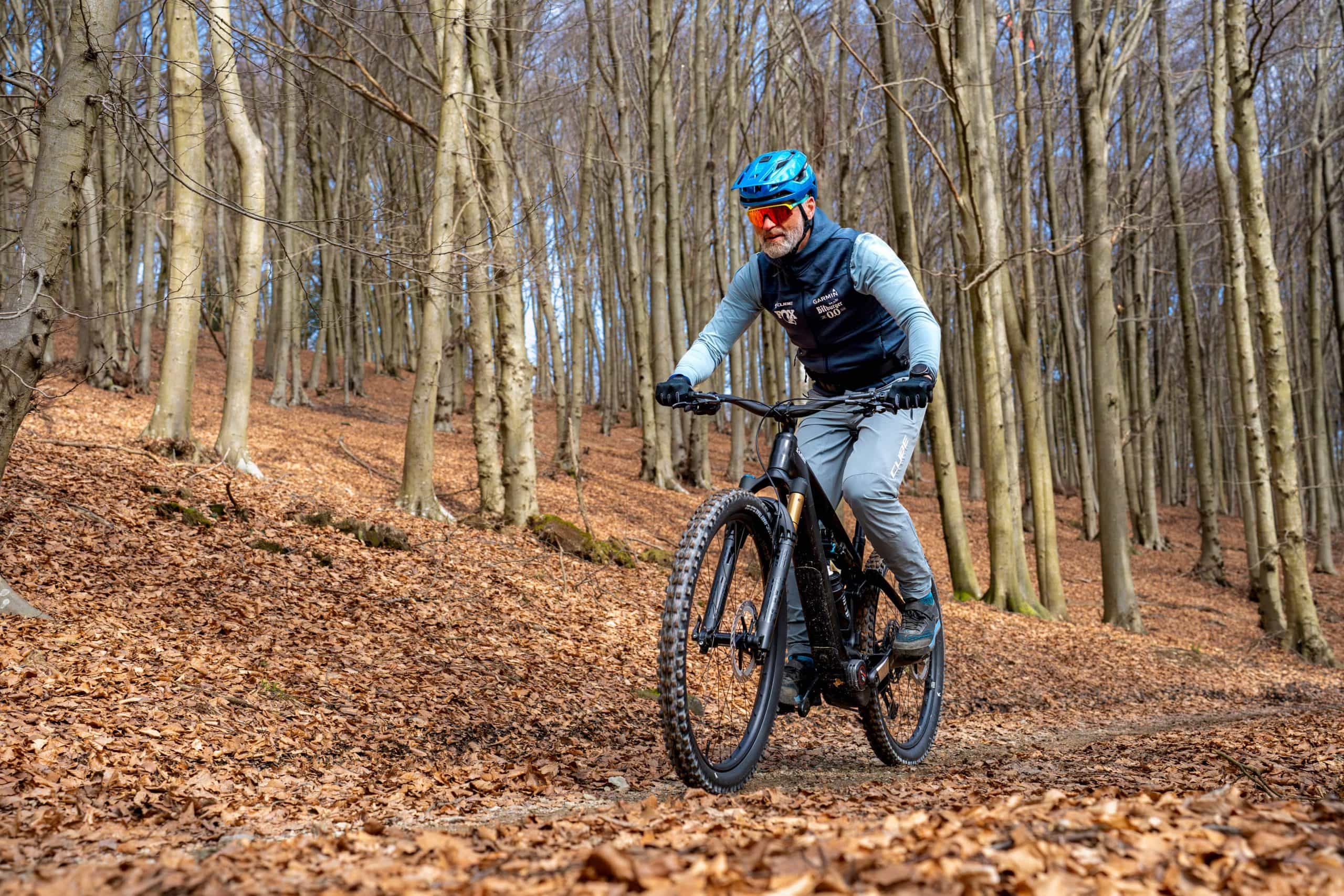 Ein Fahrer auf einem schwarzen CUBE E-Fully rollt über einen Waldweg durch einen herbstlichen Buchenwald mit dickem Laubteppich.