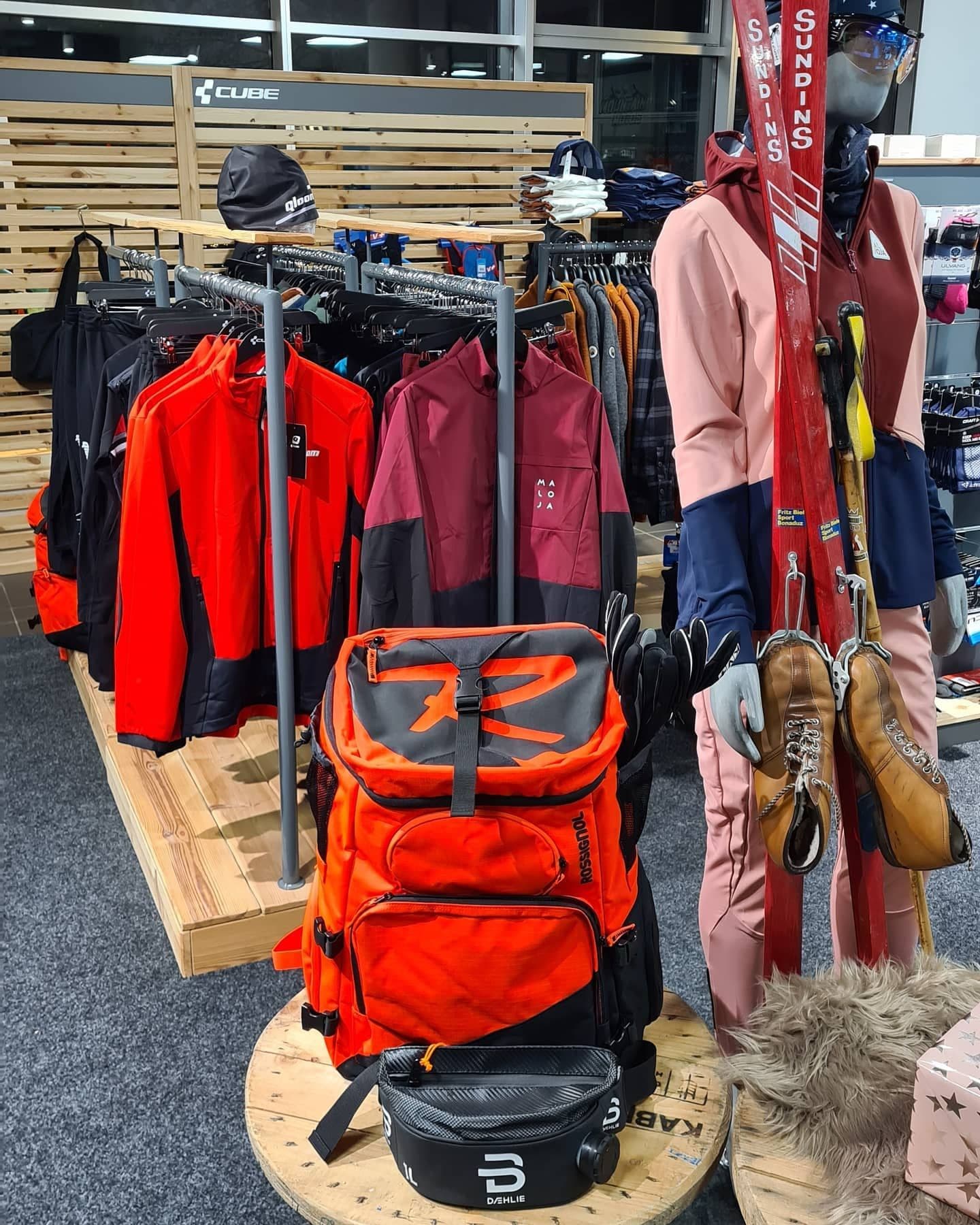 Die Nordic-Ecke im Laden mit Winterjacken auf Holzpodesten, einem orangen Skirucksack und einer Schaufensterpuppe mit alten roten Holzskiern.