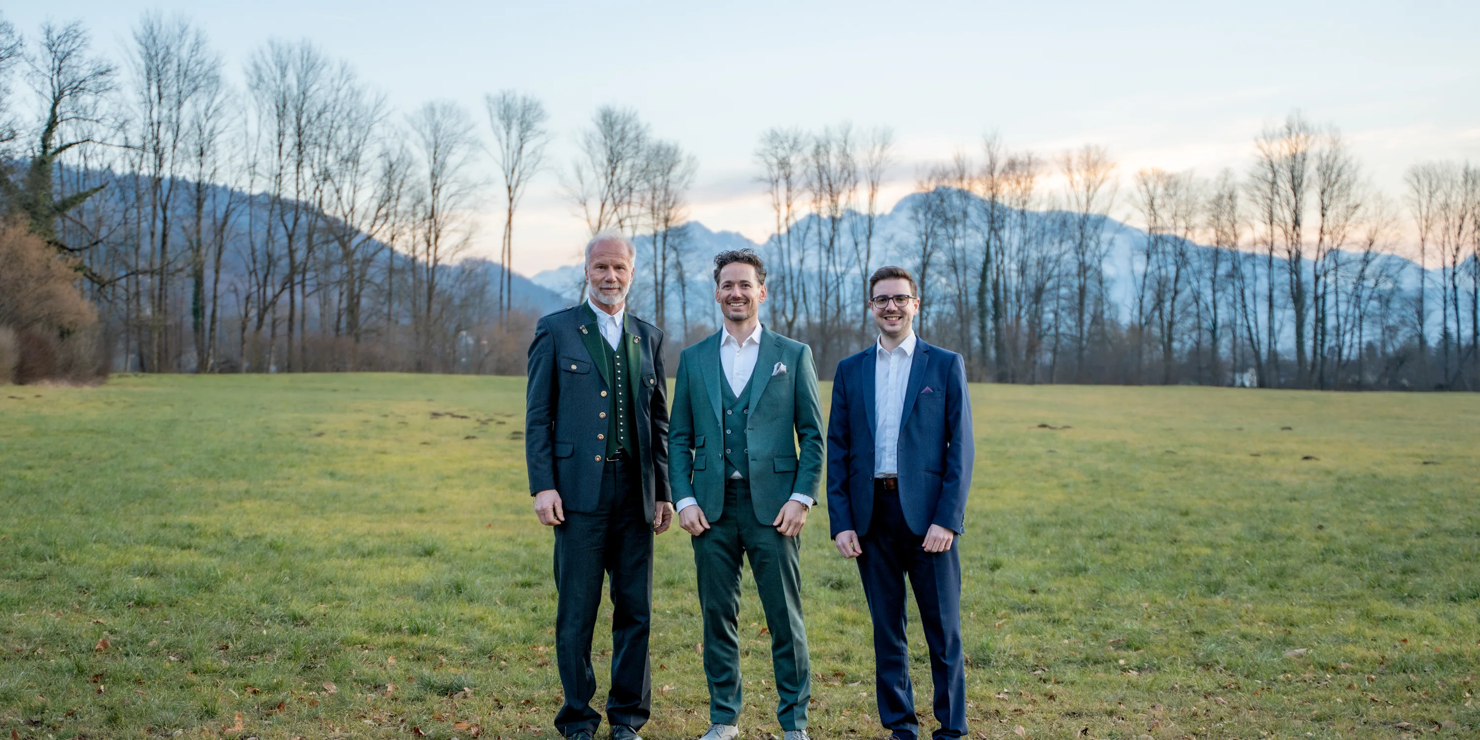 ActuQuant: Die drei Gründer stehen im Abendlicht auf einer Wiese, dahinter die Berge.