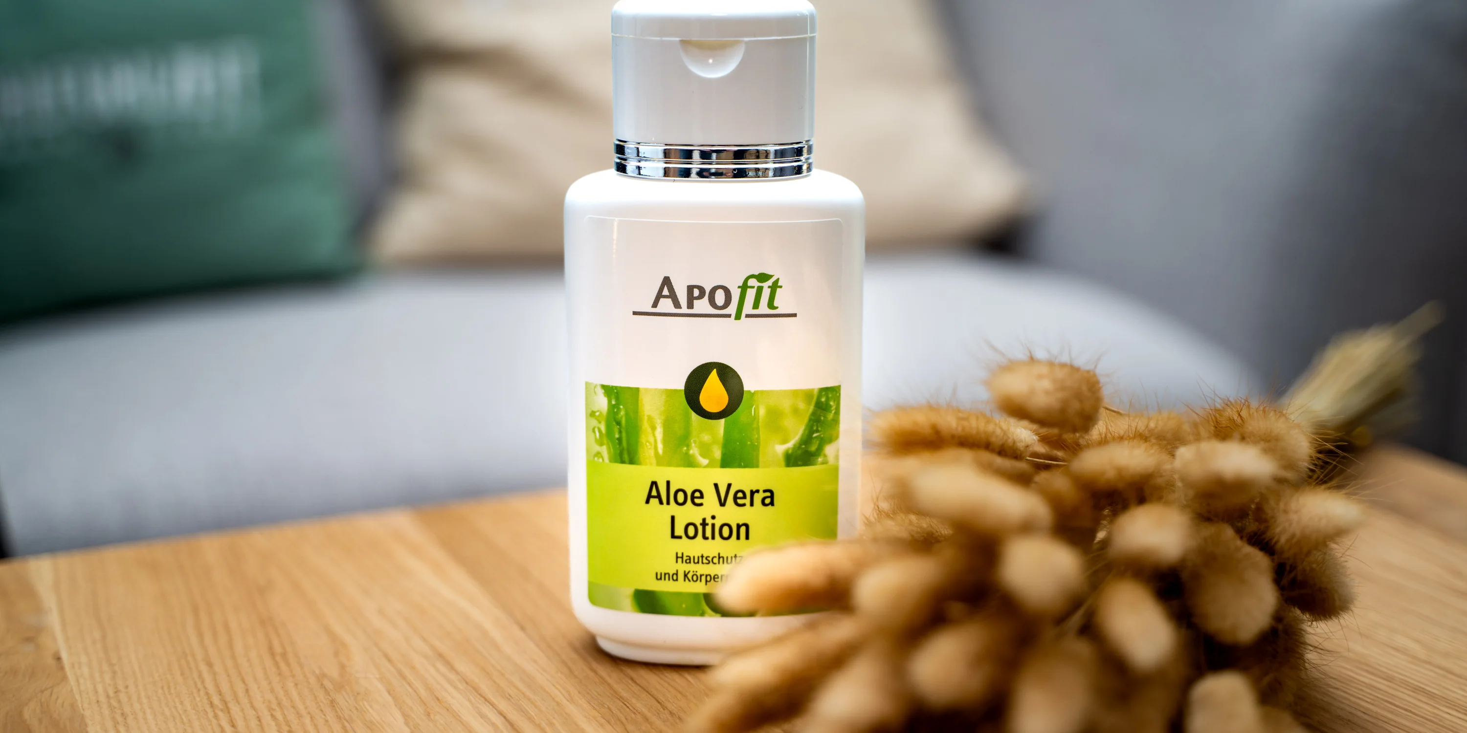 Videoproduktion für APOfit: Eine Flasche Aloe Vera Lotion steht auf einem Holztisch, daneben getrocknete Gräser.