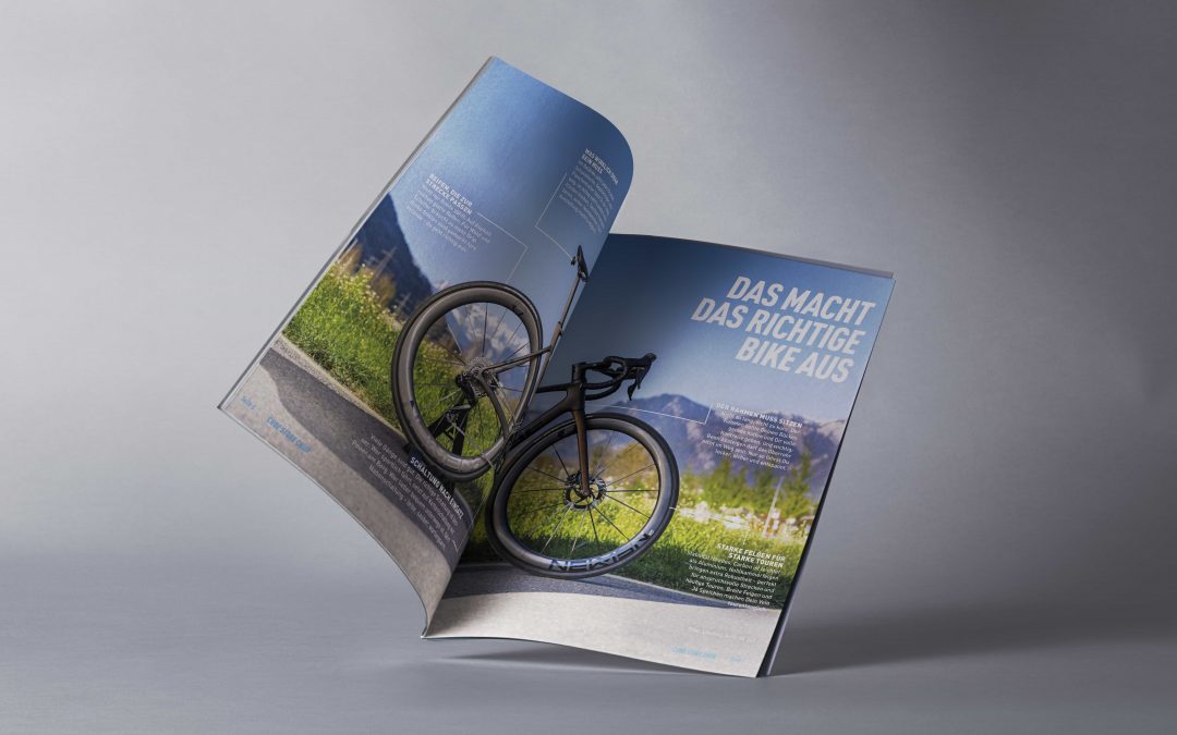 Ein aufgeschlagenes Magazin zeigt ein ganzseitiges Foto eines modernen Fahrrads auf einer malerischen Straße in der Nähe von Innsbruck, eingerahmt von Bergen. Die Schlagzeile lautet auf Deutsch „DAS MACHT DAS RICHTIGE BIKE AUS.“ und spiegelt Themen aus den Bereichen Sportmarketing und Outdoor-Abenteuer wider.