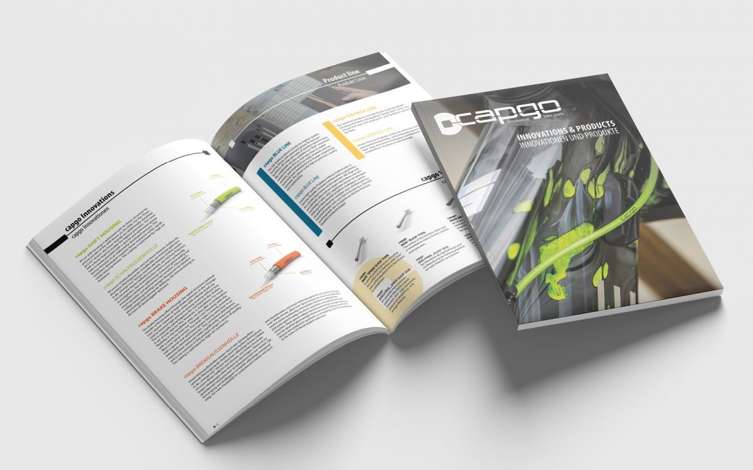 Ein Katalog mit dem Titel Cargo: Innovations & Products liegt aufgeschlagen neben dem Umschlag und zeigt Seiten mit Diagrammen, Produktbildern und farbigen Textabschnitten auf weißem Hintergrund, alles auf einer sauberen, hellen Oberfläche.