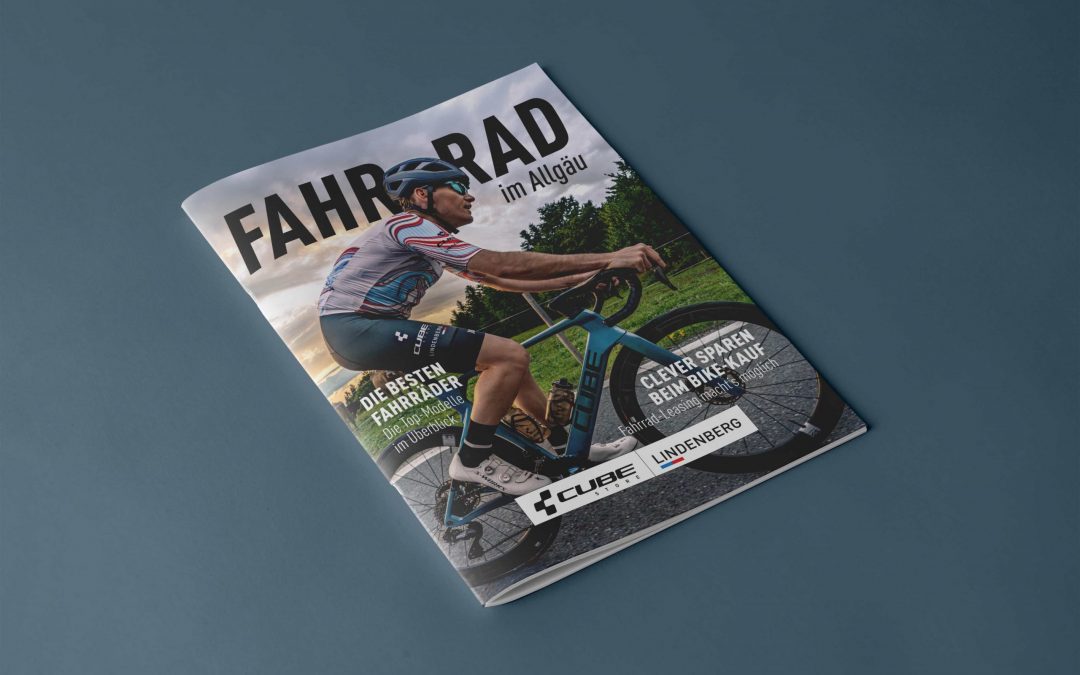 Eine Zeitschrift mit dem Titel FAHRRAD im Allgäu zeigt einen Radfahrer mit Helm und gestreiftem Trikot, der auf einer Straße fährt, mit einem malerischen, bewölkten Himmel und Bäumen im Hintergrund. Auf dem Umschlag befinden sich Werbetexte und Logos.