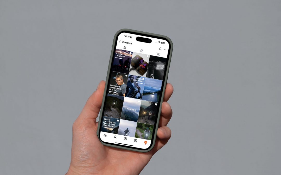 Eine Hand, die ein Smartphone hält, zeigt eine Instagram-Profilseite mit einem Raster von Fotos, die Aktivitäten im Freien und Abenteuerszenen vor einem schlichten grauen Hintergrund zeigen.