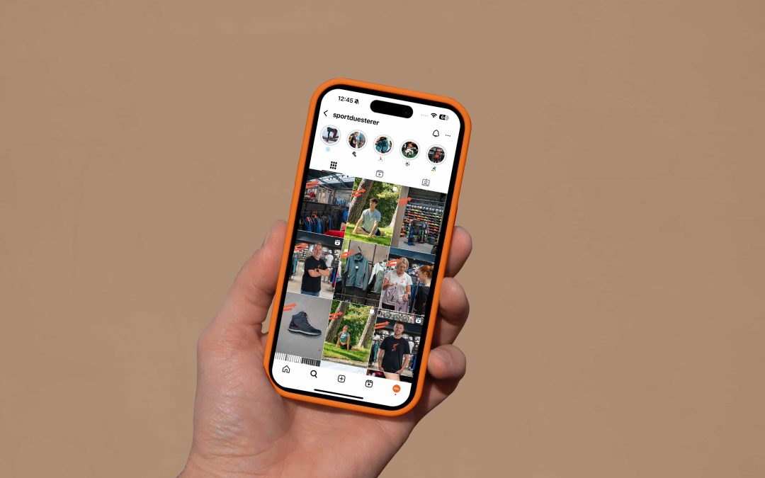 Eine Hand, die ein Smartphone hält, zeigt eine Instagram-Profilseite mit einem Raster von Fotos, darunter Menschen, Turnschuhe und Szenen im Freien, vor einem schlichten beigen Hintergrund.