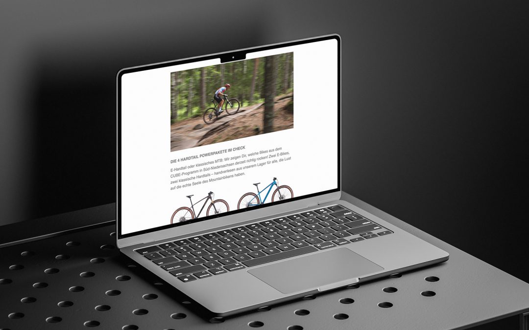 Ein Laptop auf einer perforierten Metalloberfläche zeigt eine Webseite mit Bildern und Beschreibungen von Fahrrädern an, mit einem unscharfen Waldhintergrund in einem Bild. Die Umgebung hat eine schlichte, moderne, monochrome Ästhetik.
