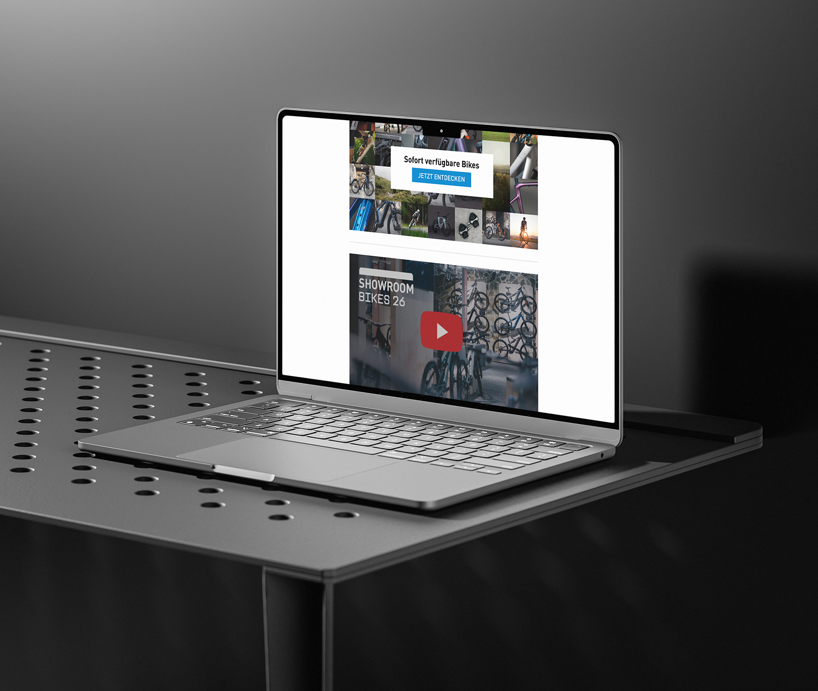 Ein Laptop auf einem perforierten Metalltisch zeigt eine Website mit Fahrrädern, eine blaue Schaltfläche für die Aufforderung zum Handeln und eine Videominiaturansicht mit Fahrrädern in einem Ausstellungsraum. Der Hintergrund ist dunkel und minimalistisch.