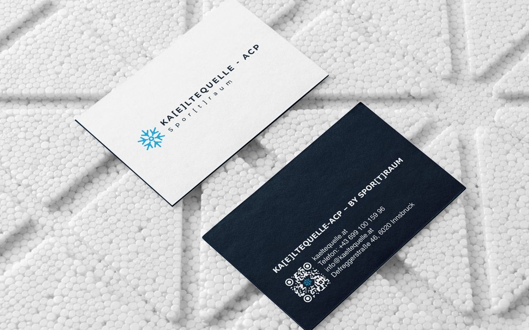 Zwei Visitenkarten, eine weiße und eine dunkelblaue, zeigen das Logo und die Kontaktdaten von KAELTEQUELLE-ACP. Die weiße Karte liegt mit der Vorderseite nach oben, die blaue Karte mit dem QR-Code mit der Rückseite nach unten, beide auf einer strukturierten weißen Oberfläche.