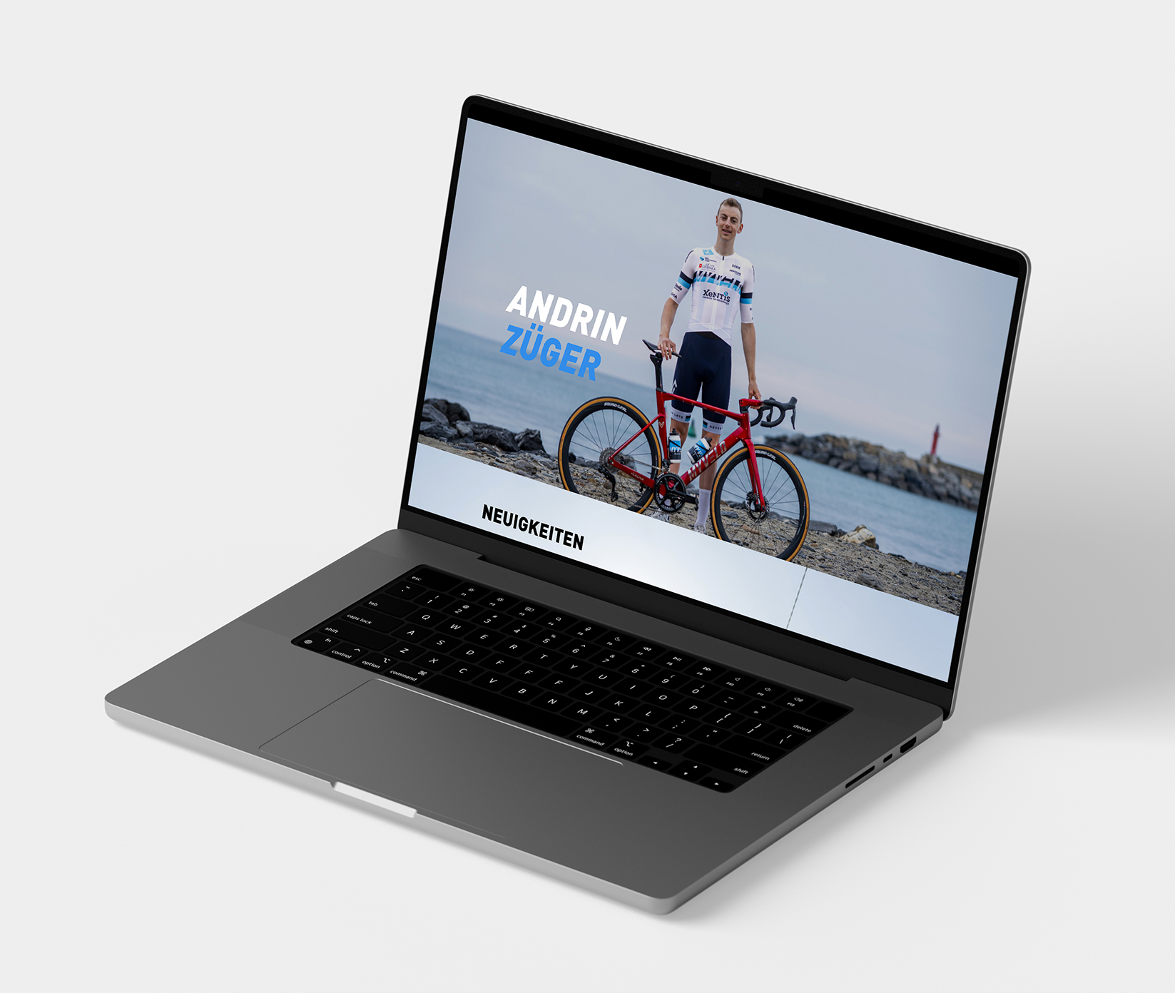 AndrinZueger_Portfolio_Mockup Ein Laptop, auf dem eine Website mit einem Radfahrer angezeigt wird, der neben einem roten Fahrrad an einem felsigen Ufer steht, wobei der Name Andrin Züger und das Wort Neuigkeiten auf dem Bildschirm zu sehen sind.