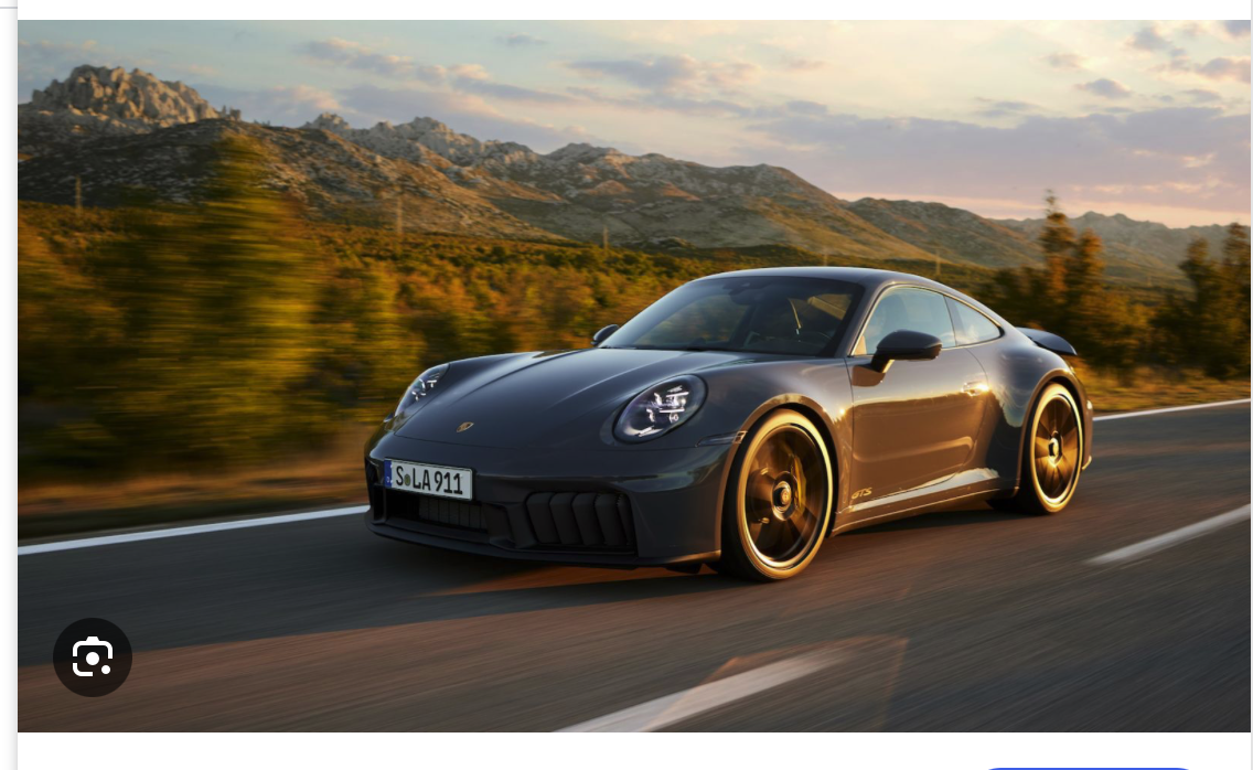 Ein schnittiger, dunkelgrauer Porsche-Sportwagen fährt auf einer offenen Straße mit verschwommenen Bäumen und felsigen Bergen im Hintergrund bei Sonnenuntergang.