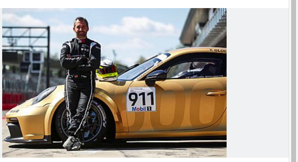 Ein Rennfahrer in einem schwarzen Rennanzug steht mit verschränkten Armen an einen goldenen Porsche-Rennwagen mit der Nummer 911 gelehnt. Ein Rennhelm liegt auf dem Autodach; sie befinden sich an einem sonnigen Tag auf einer Rennstrecke.