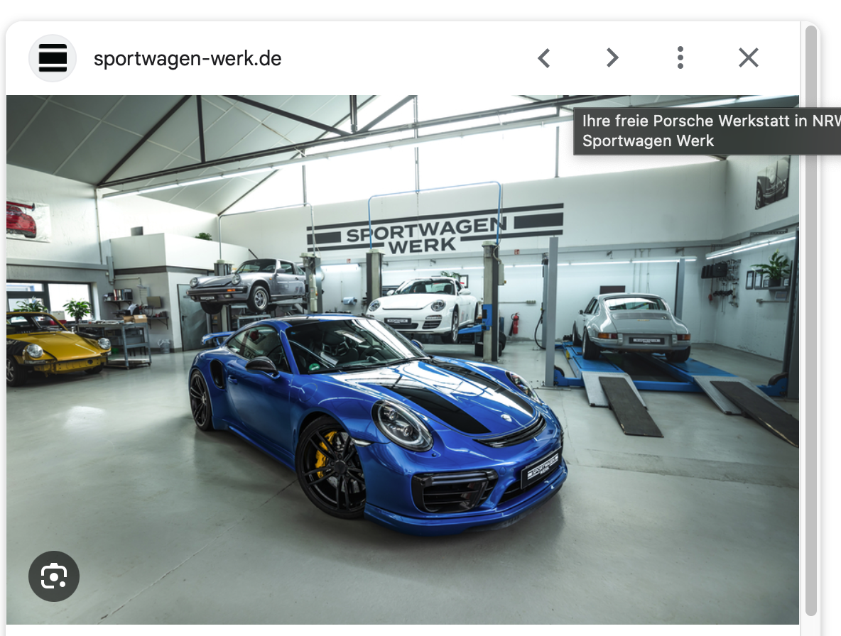 Ein glänzender blauer Porsche-Sportwagen steht in einer sauberen, modernen Autowerkstatt, in der mehrere andere Autos auf Hebebühnen stehen. Große Fenster lassen natürliches Licht herein, und an der Rückwand hängt ein Schild mit der Aufschrift SPORTWAGEN WERK.