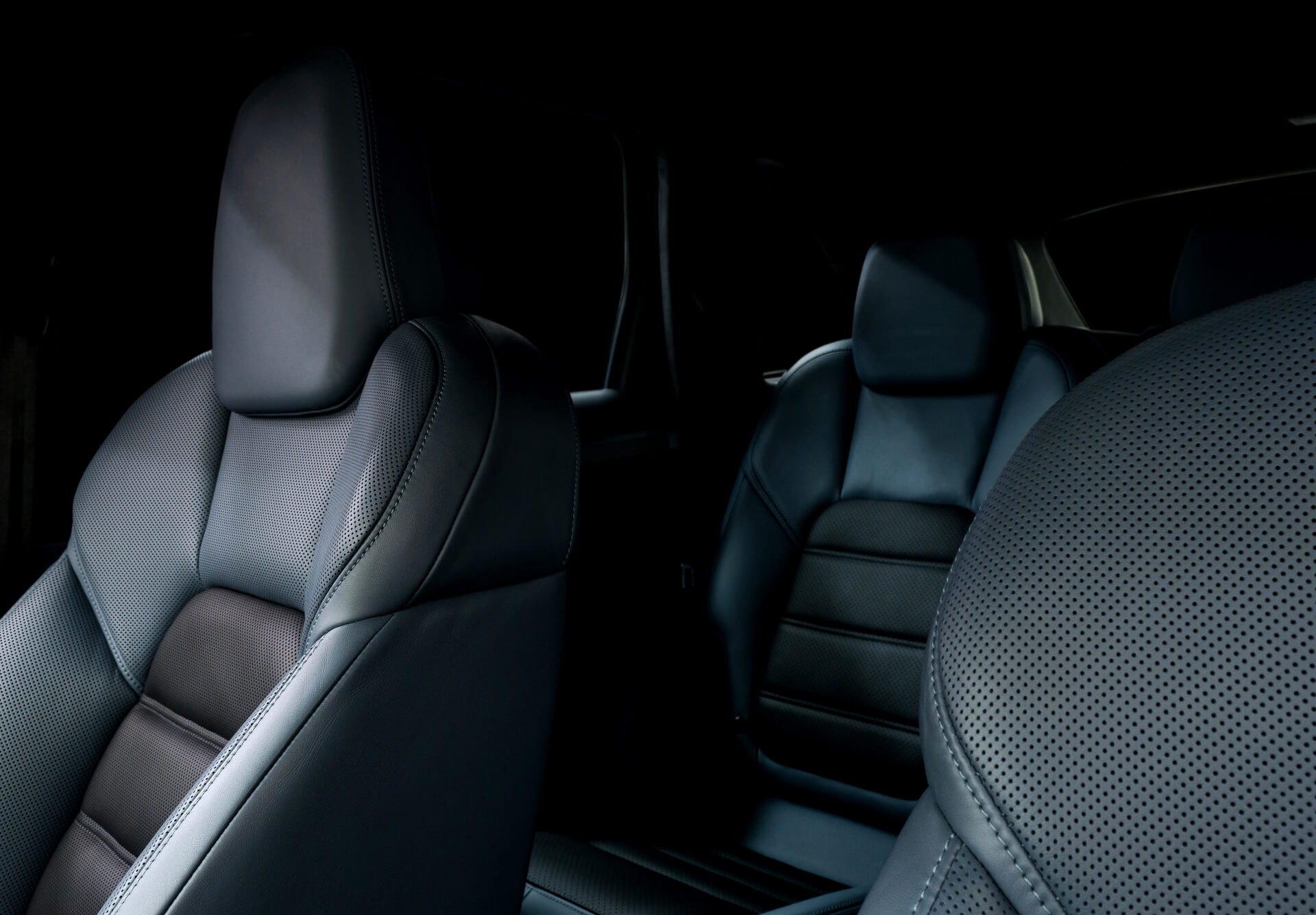 Nahaufnahme von schwarzen Ledersitzen mit detaillierten Nähten und perforierten Mustern in einem dunklen, modernen Fahrzeuginnenraum.