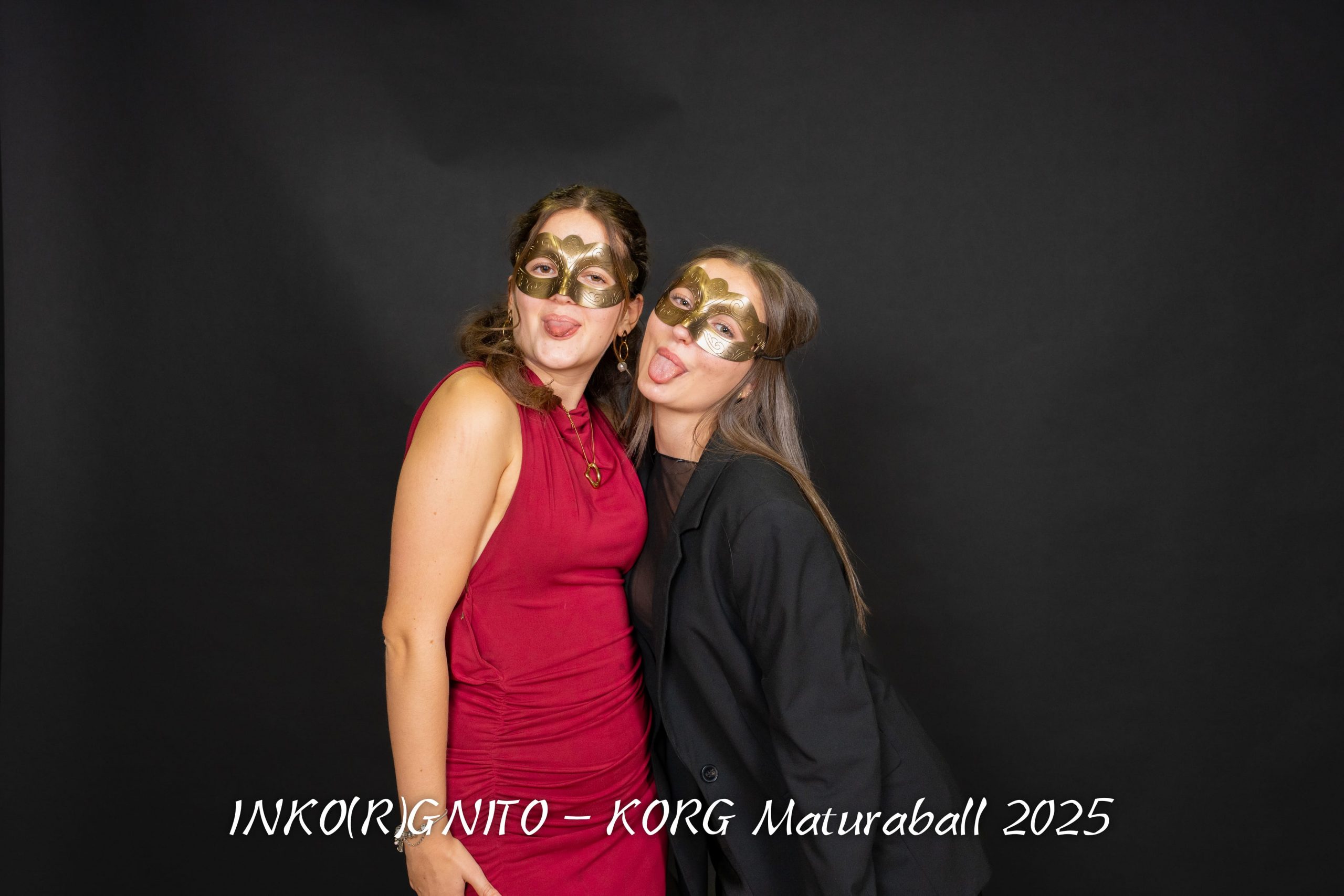 Zwei maskierte Personen posieren spielerisch vor einem schwarzen Hintergrund, beide strecken ihre Zungen heraus. Die eine trägt ein rotes Kleid, die andere ein schwarzes Outfit. Der weiße Text am unteren Rand lautet: INKOIRGNITO - KORG Maturaball 2025.